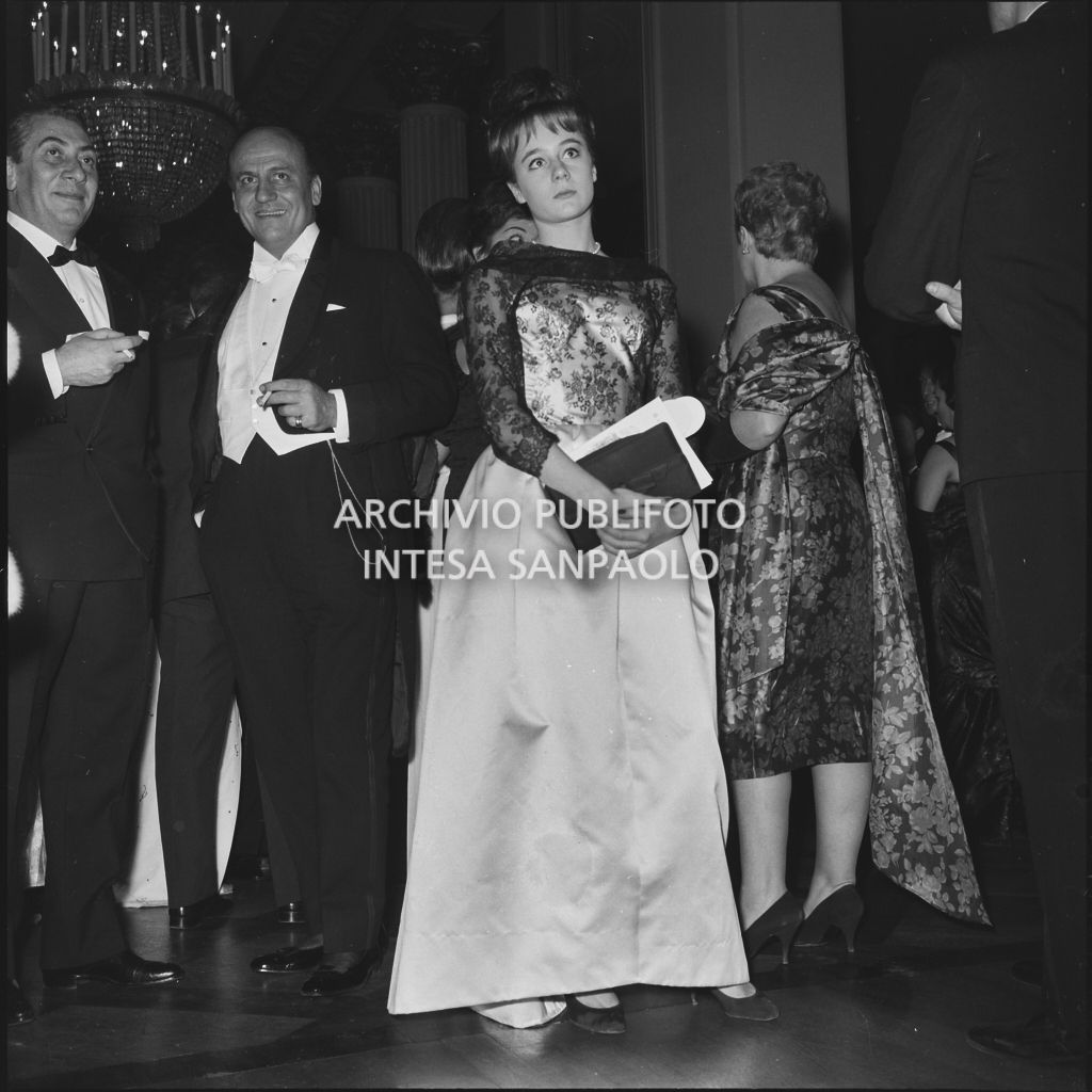 Lo stilista Pierre Balmain ed altri spettatori nel foyer del Teatro alla Scala in occasione della serata inaugurale della stagione lirica 1961-1962 con l'opera "La battaglia di Legnano" di Giuseppe Verdi, diretta da Gianandrea Gavazzeni con la regia di Margherita Wallmann