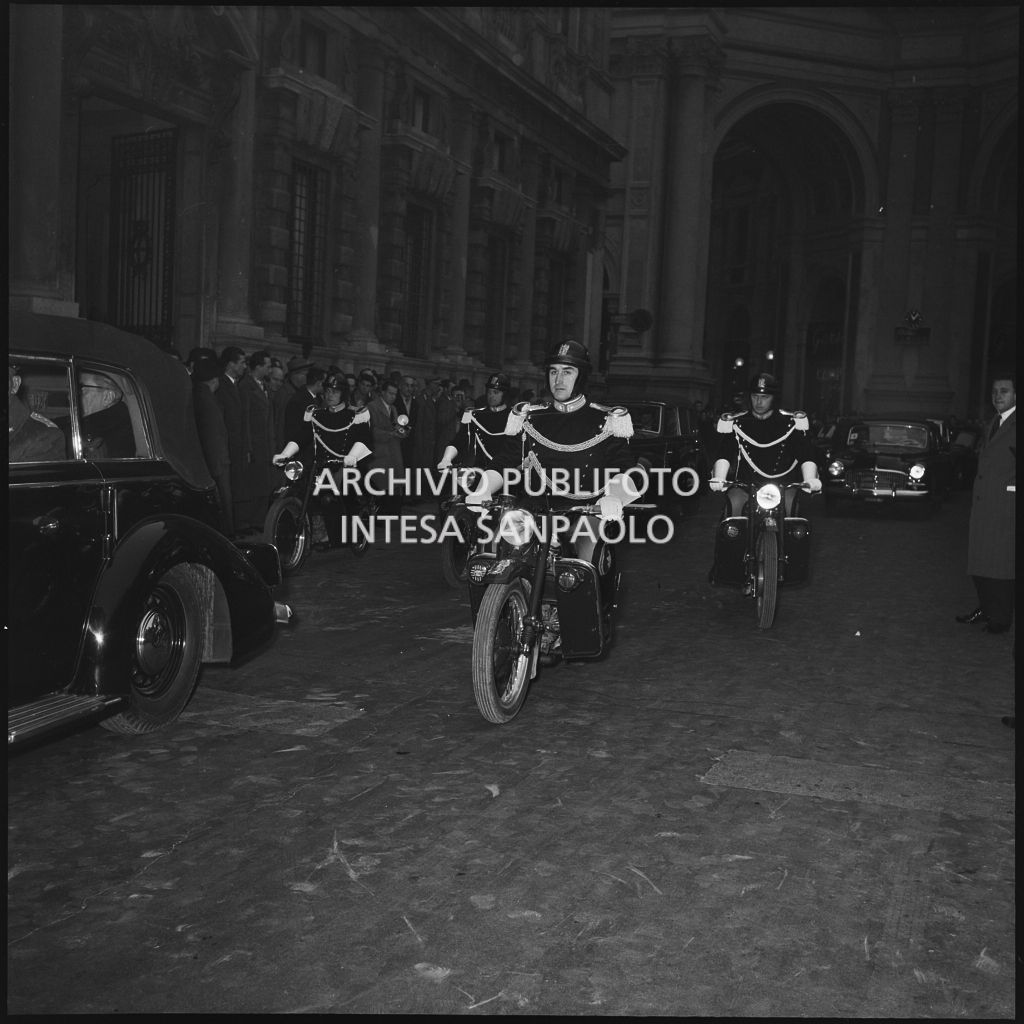 Corazzieri in motocicletta scortano l'automobile presidenziale, con a bordo Giovanni Gronchi, al Teatro alla Scala per assistere alla serata inaugurale della stagione lirica 1955-1956 con l'opera "Norma" di Vincenzo Bellini, diretta da Antonino Votto, con la regia di Margherita Wallmann