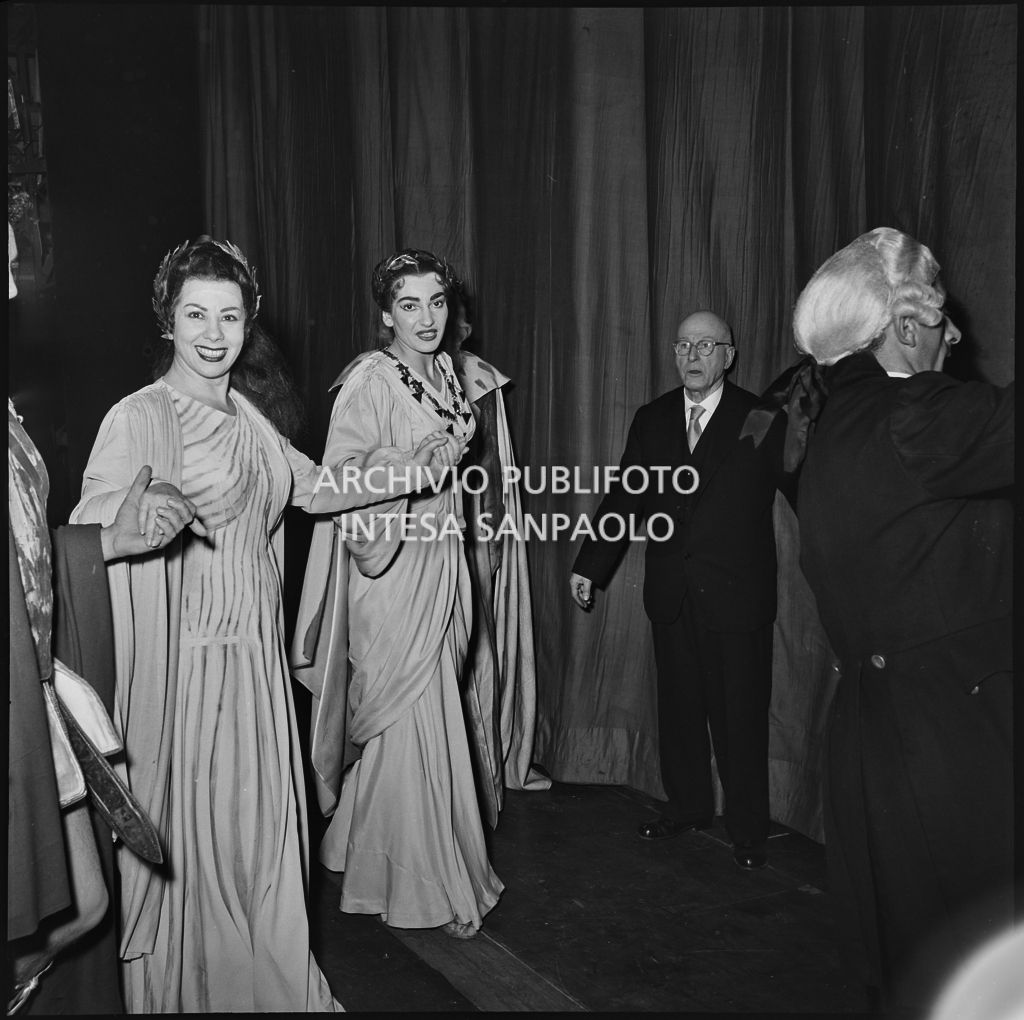 Da sinistra, il mezzosoprano Giulietta Simionato e la soprano Maria Callas, in costumi di scena, dietro al sipario del Teatro alla Scala, al termine della rappresentazione dell'opera "Norma" di Vincenzo Bellini, diretta da Antonino Votto, con la regia di Margherita Wallmann, che inaugura la stagione lirica 1955-1956