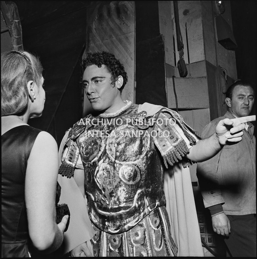 Il tenore Mario Del Monaco, in abiti di scena, parla con una donna dietro le quinte del Teatro alla Scala durante la serata inaugurale della stagione lirica 1955-1956 con l'opera "Norma" di Vincenzo Bellini, diretta da Antonino Votto, con la regia di Margherita Wallmann