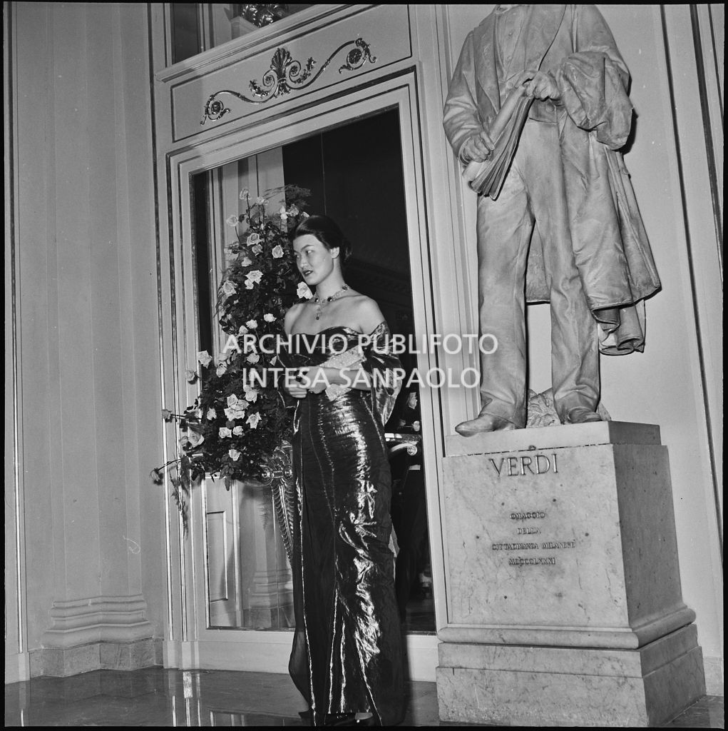 La signora Pao Veneziani in posa accanto alla statua di Giuseppe Verdi, al Teatro alla Scala in occasione della serata inaugurale della stagione lirica 1955-1956 con l'opera "Norma" di Vincenzo Bellini, diretta da Antonino Votto, con la regia di Margherita Wallmann