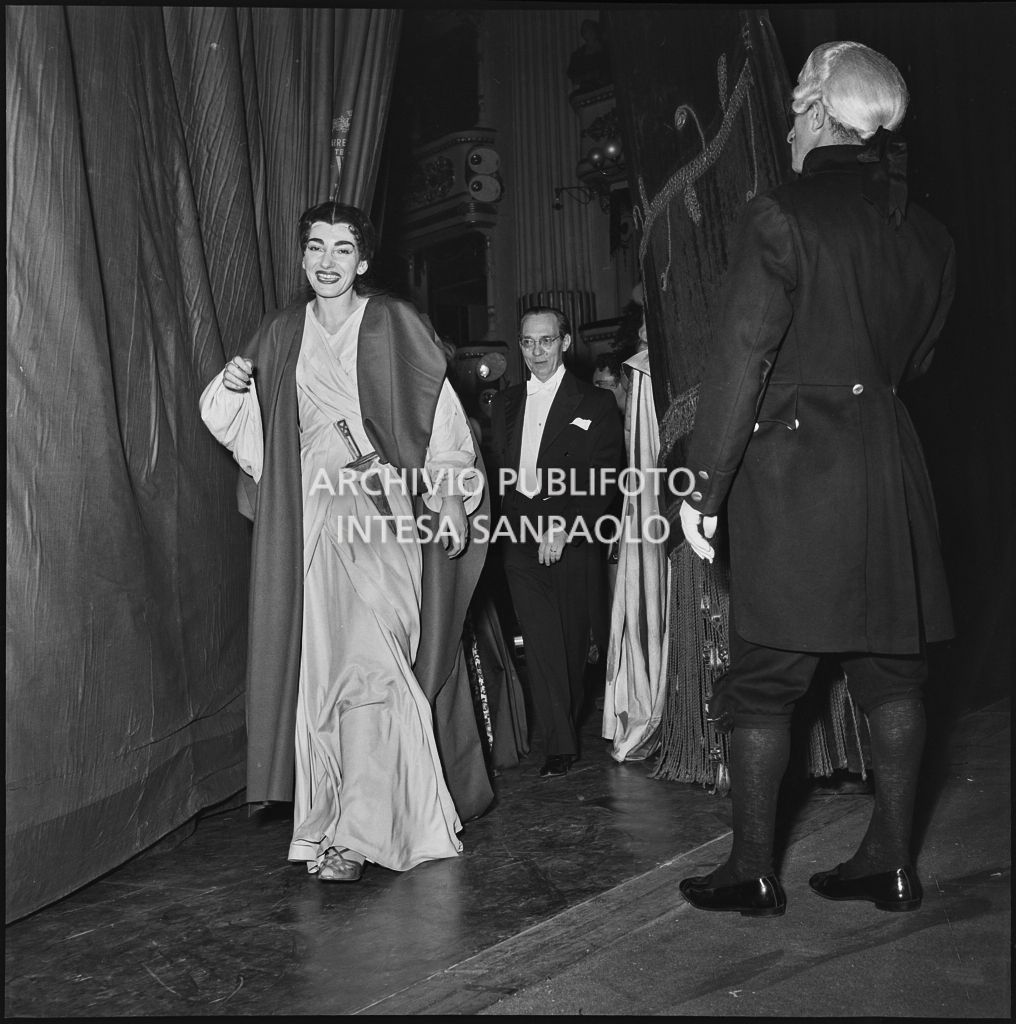 La soprano Maria Callas, in abiti di scena, e il direttore d'orchestra Antonino Votto dietro al sipario del Teatro alla Scala al termine della rappresentazione dell'opera "Norma" di Vincenzo Bellini, diretta da Antonino Votto, con la regia di Margherita Wallmann, che inaugura la stagione lirica 1955-1956