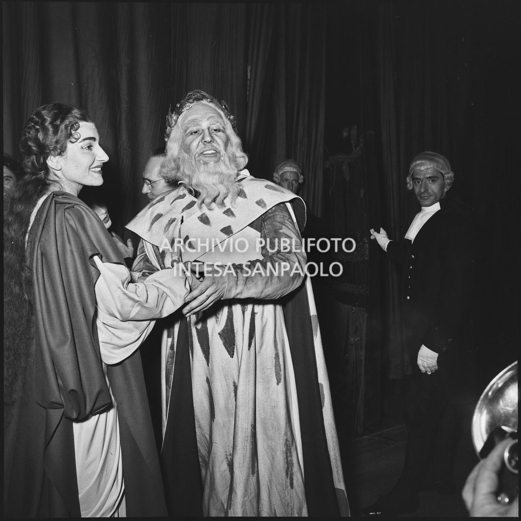 La soprano Maria Callas e il basso Nicola Zaccaria, in abiti di scena, posano davanti ai fotografi dietro al sipario del Teatro alla Scala, al termine della rappresentazione dell'opera "Norma" di Vincenzo Bellini, diretta da Antonino Votto, con la regia di Margherita Wallmann, che inaugura la stagione lirica 1955-1956