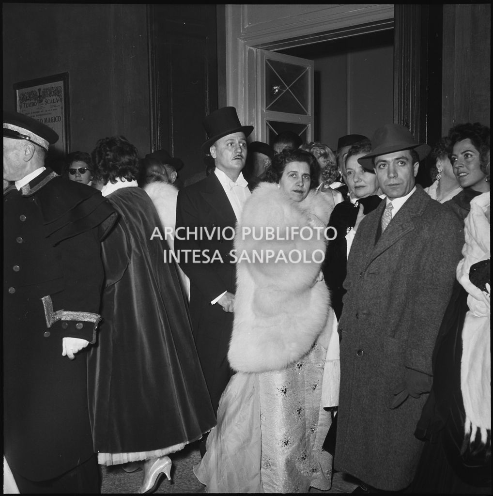 Lo stilista Pierre Balmain tra la folla di spettatori nella galleria delle carrozze del Teatro alla Scala in occasione della serata inaugurale della stagione lirica 1955-1956 con l'opera "Norma" di Vincenzo Bellini, diretta da Antonino Votto, con la regia di Margherita Wallmann