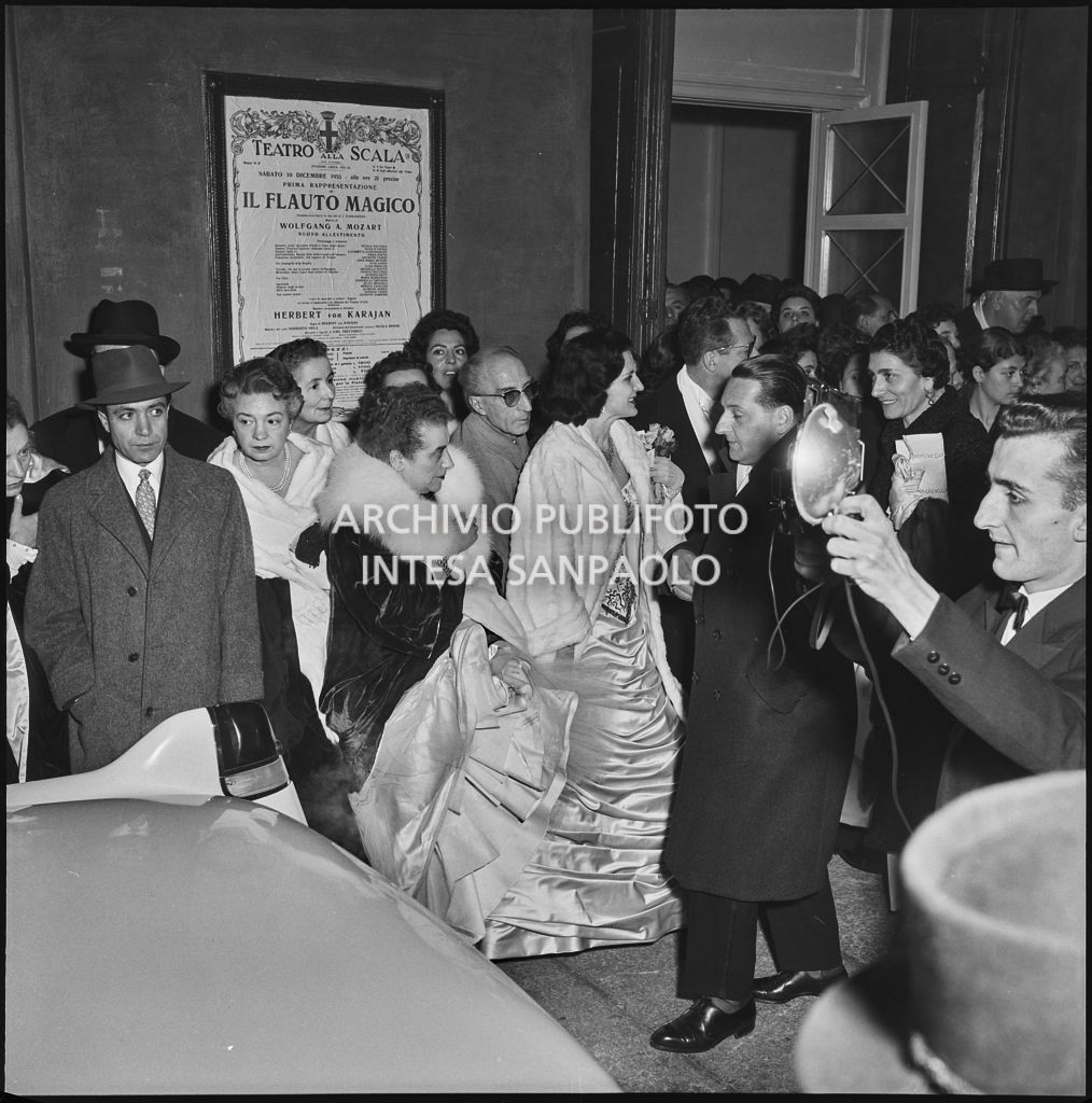 La signora Bracco tra spettatori e fotografi nella galleria delle carrozze del Teatro alla Scala in occasione della serata inaugurale della stagione lirica 1955-1956 con l'opera "Norma" di Vincenzo Bellini, diretta da Antonino Votto, con la regia di Margherita Wallmann