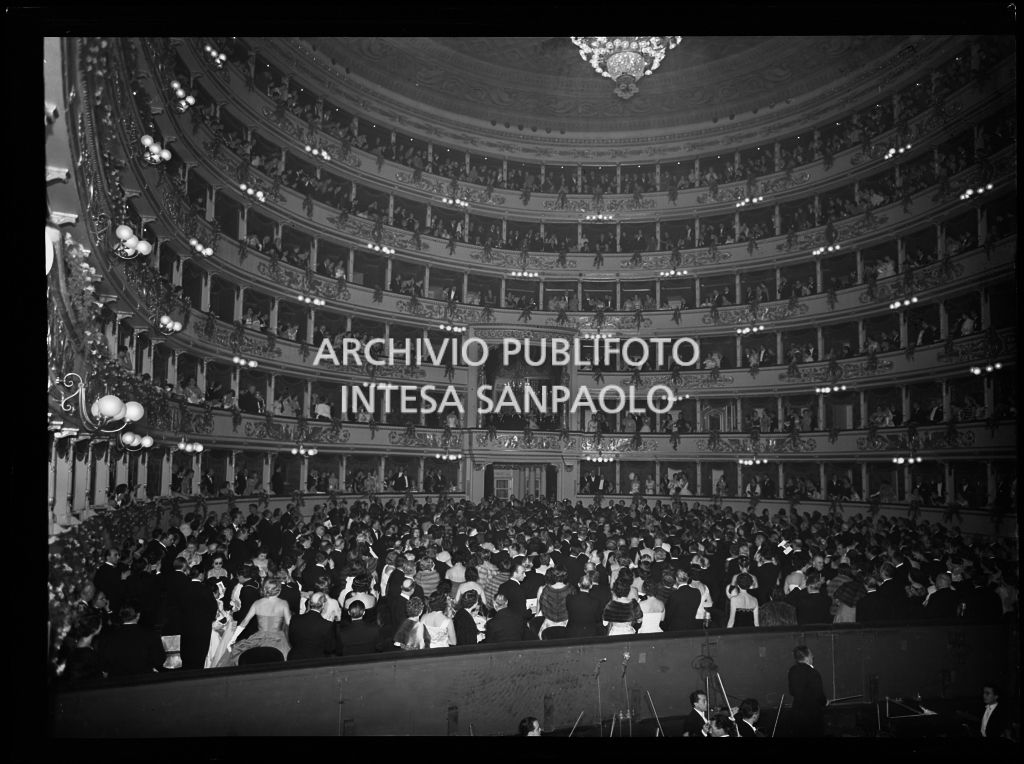 Vista dal palcoscenico del Teatro alla Scala sulla sala, gremita di gente, durante l'esecuzione dell'inno nazionale italiano in occasione della serata inaugurale della stagione lirica 1955-1956 con l'opera "Norma" di Vincenzo Bellini, diretta da Antonino Votto, con la regia di Margherita Wallmann