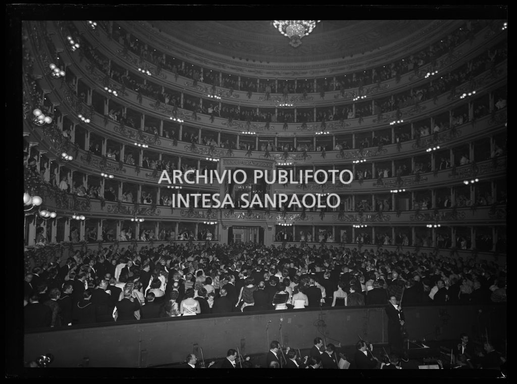 Vista dal palcoscenico del Teatro alla Scala sulla sala, gremita di gente, durante l'esecuzione dell'inno nazionale italiano in occasione della serata inaugurale della stagione lirica 1955-1956 con l'opera "Norma" di Vincenzo Bellini, diretta da Antonino Votto, con la regia di Margherita Wallmann