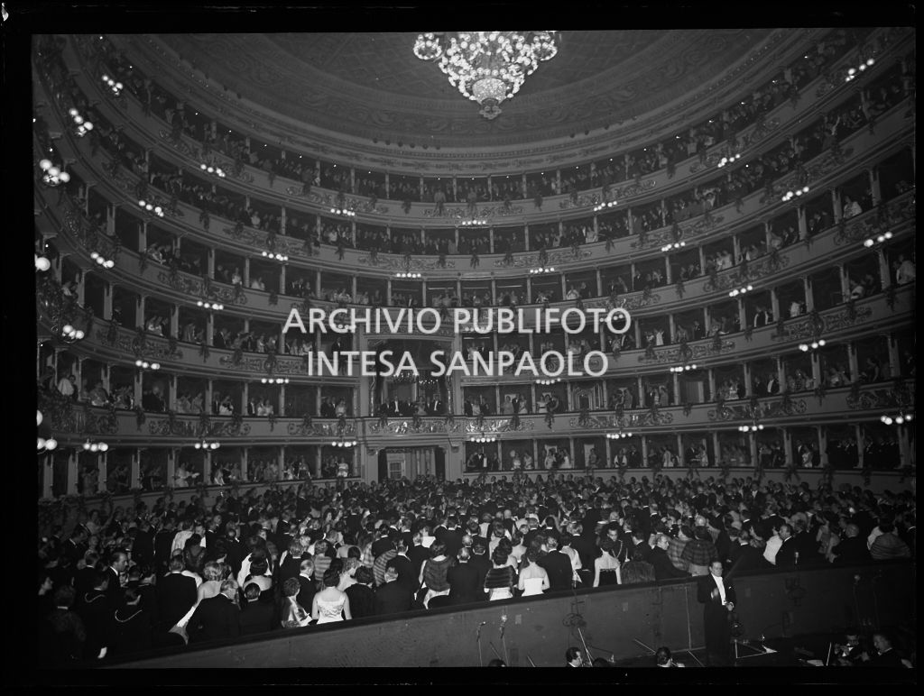 Vista dal palcoscenico del Teatro alla Scala sulla sala, gremita di gente, durante l'esecuzione dell'inno nazionale italiano in occasione della serata inaugurale della stagione lirica 1955-1956 con l'opera "Norma" di Vincenzo Bellini, diretta da Antonino Votto, con la regia di Margherita Wallmann