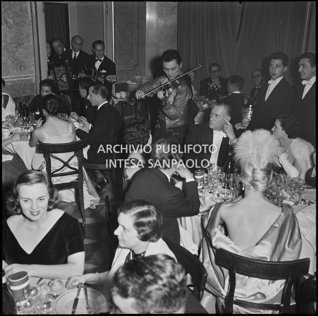 Barbara Balmain, di spalle, ed altri spettatori alla cena dopo l'inaugurazione della stagione lirica 1956-1957 del Teatro alla Scala con l'opera "Aida" di Giuseppe Verdi, diretta da Antonino Votto, con la regia di Franco Enriquez