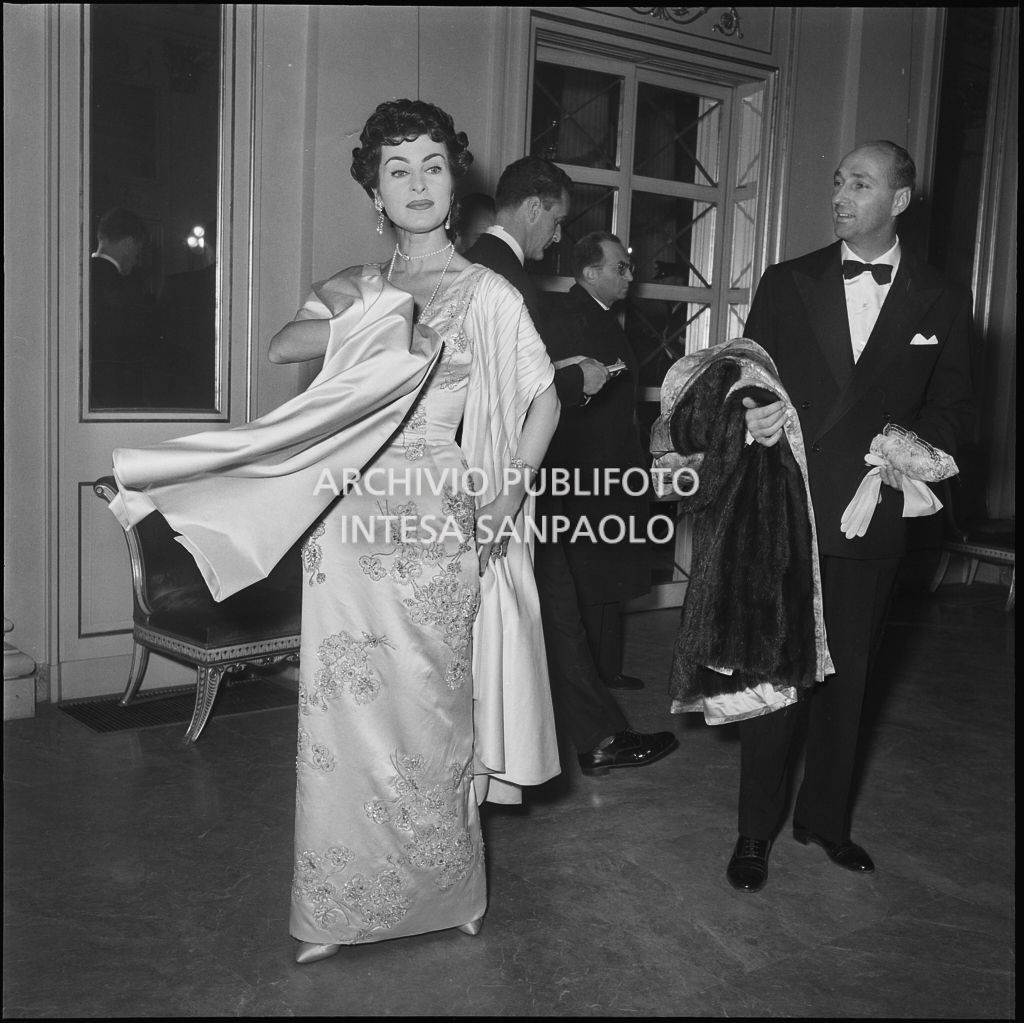 Silvana Pampanini mostra il suo abito nel foyer del Teatro alla Scala in occasione dell'inaugurazione della stagione lirica 1956-1957 con l'opera "Aida" di Giuseppe Verdi, diretta da Antonino Votto, con la regia di Franco Enriquez