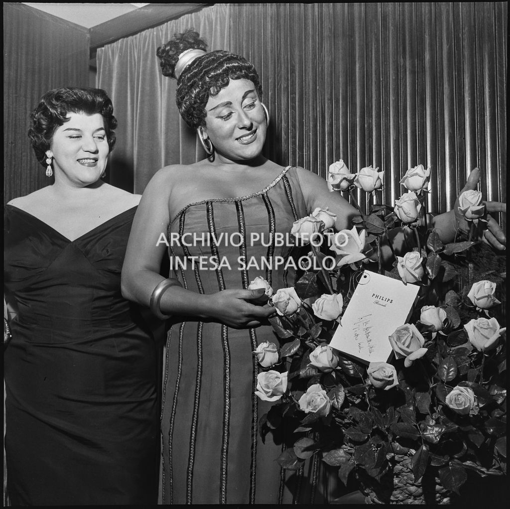 Il soprano Antonietta Stella, in abiti di scena, con un mazzo di rose regalatole dalla Philips Records e Emilia Carlini al Teatro alla Scala in occasione dell'inaugurazione della stagione lirica 1956-1957 con l'opera "Aida" di Giuseppe Verdi, diretta da Antonino Votto, con la regia di Franco Enriquez