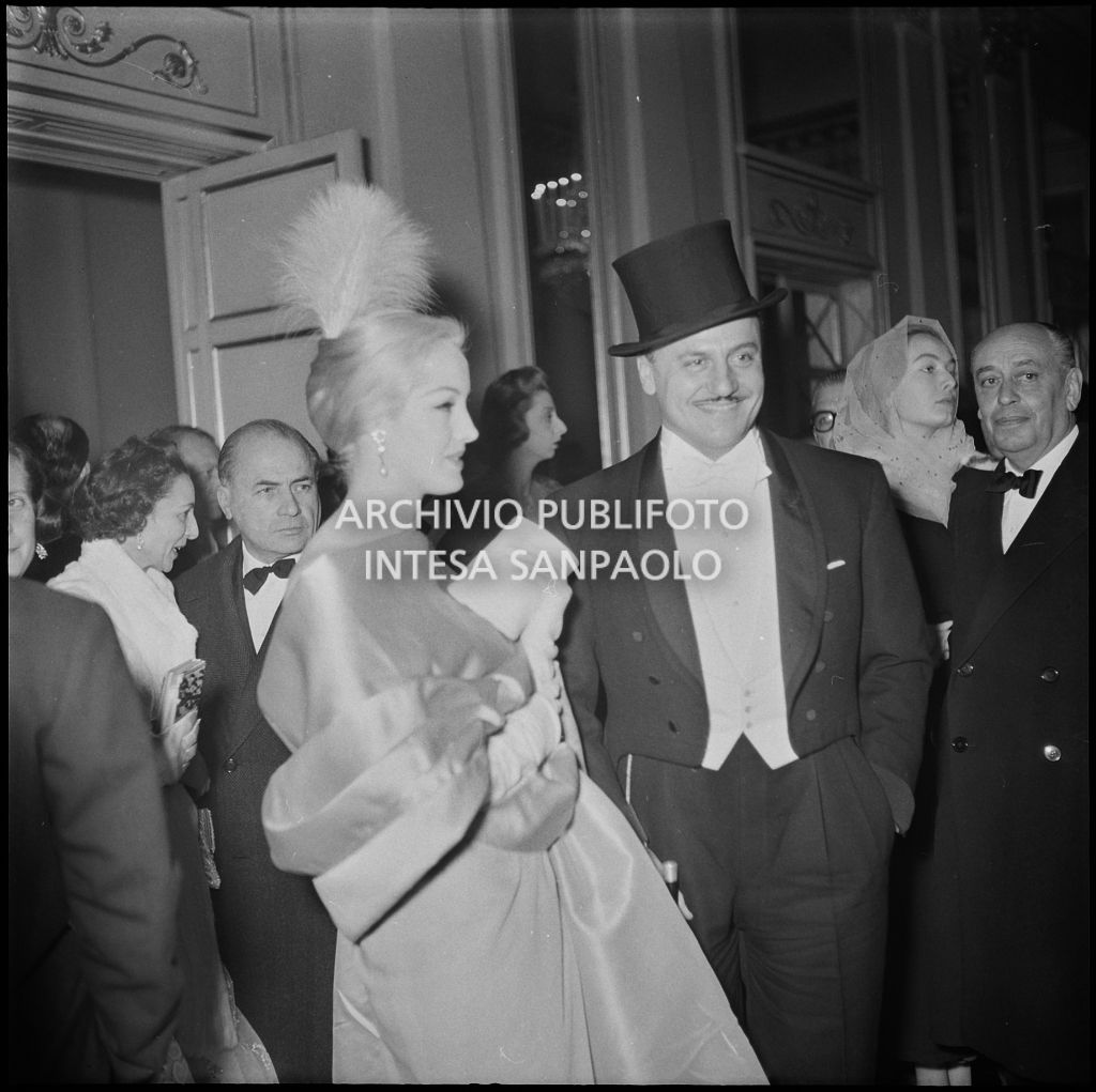 Lo stilista Pierre Balmain e Barbara Balmain nel foyer del Teatro alla Scala in occasione dell'inaugurazione della stagione lirica 1956-1957 con l'opera "Aida" di Giuseppe Verdi, diretta da Antonino Votto, con la regia di Franco Enriquez