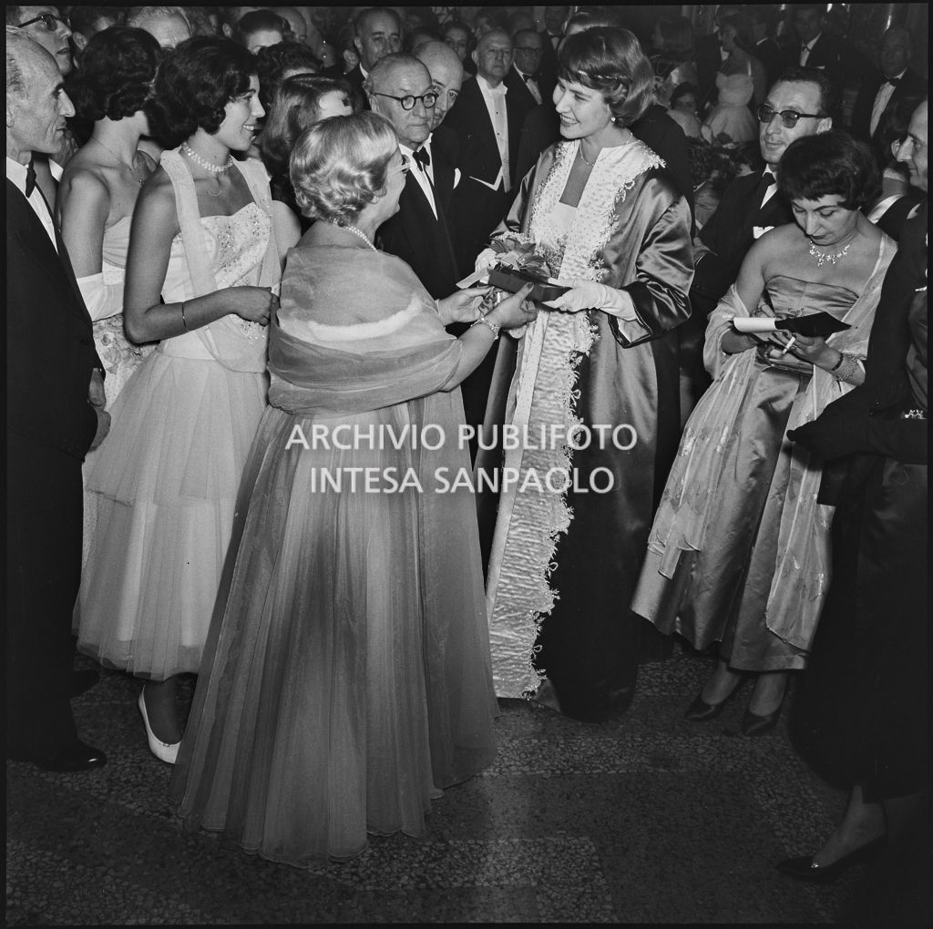 Jole Veneziani consegna un pacchetto a Rita Cook nel foyer del Teatro alla Scala in occasione della serata inaugurale della stagione lirica 1957-1958 con l'opera "Un ballo in maschera", di Giuseppe Verdi, diretta da Gianandrea Gavazzeni con la regia di Margherita Wallmann
