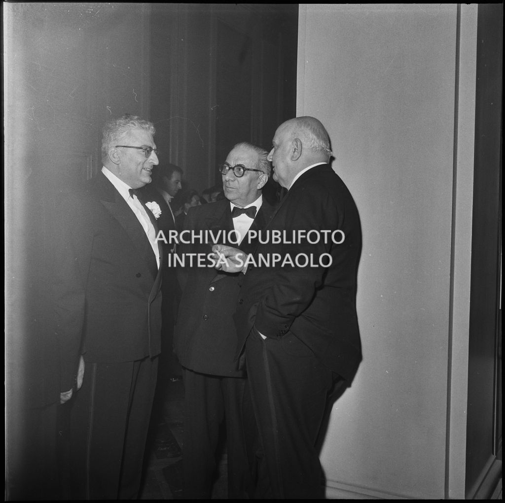 Tre spettatori discutono nel foyer del Teatro alla Scala in occasione della serata inaugurale della stagione lirica 1957-1958 con l'opera "Un ballo in maschera", di Giuseppe Verdi, diretta da Gianandrea Gavazzeni con la regia di Margherita Wallmann