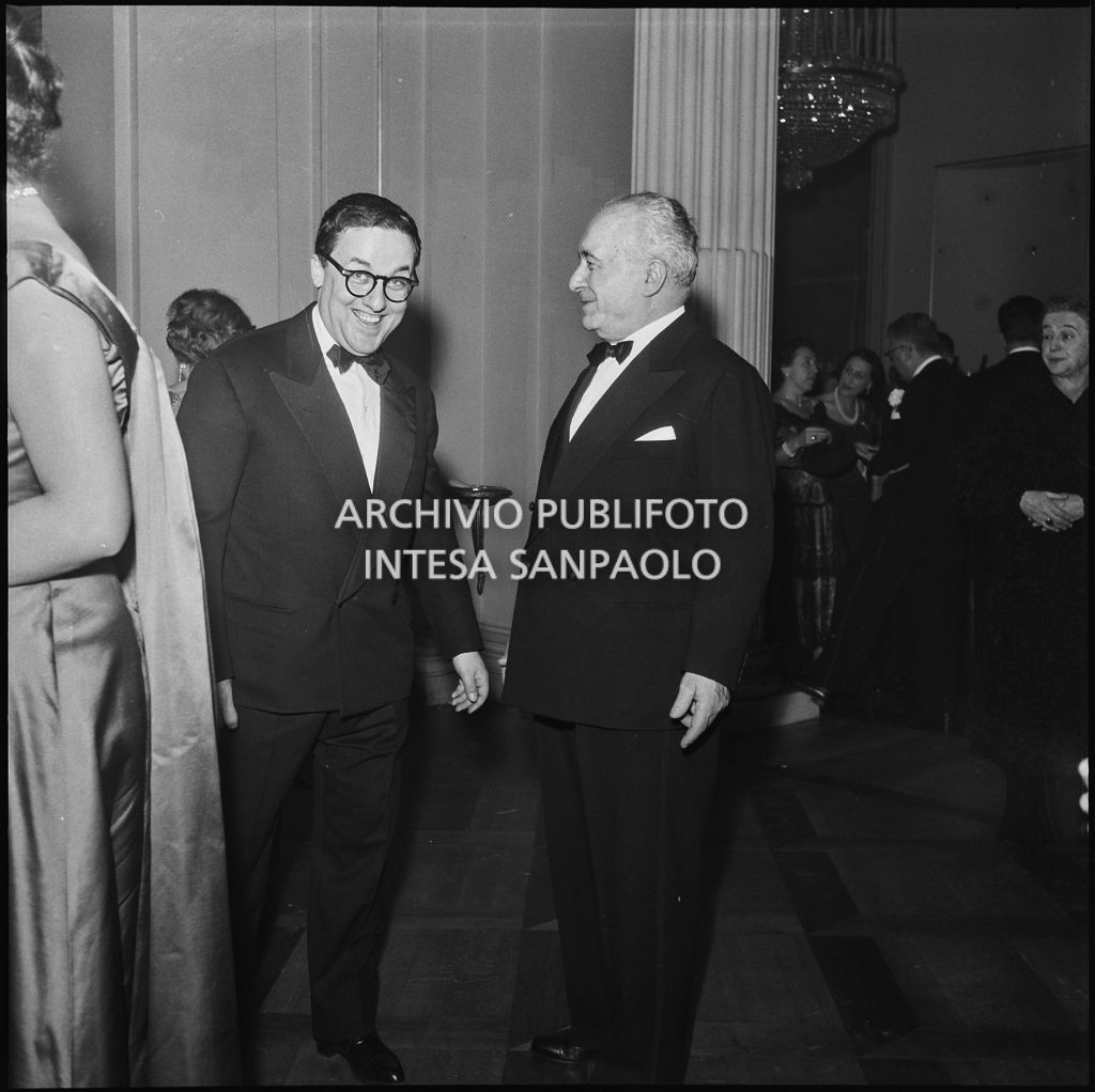 Il ministro del Lavoro e della Previdenza Sociale Ezio Vigorelli in compagnia di un altro spettatore nel foyer del Teatro alla Scala in occasione della serata inaugurale della stagione lirica 1957-1958 con l'opera "Un ballo in maschera", di Giuseppe Verdi, diretta da Gianandrea Gavazzeni con la regia di Margherita Wallmann