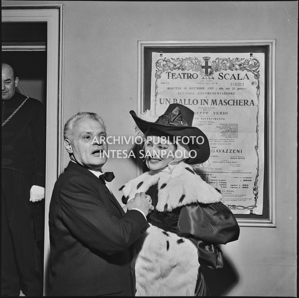 Il soprintendente del Teatro alla Scala Antonio Ghringhelli e la soprano Maria Callas, in costume di scena, ritratti in teatro, davanti alla locandina di "Un ballo in maschera" la sera dell'inaugurazione della stagione lirica 1957-1958 con l'opera di Giuseppe Verdi, diretta da Gianandrea Gavazzeni e con la regia di Margherita Wallmann