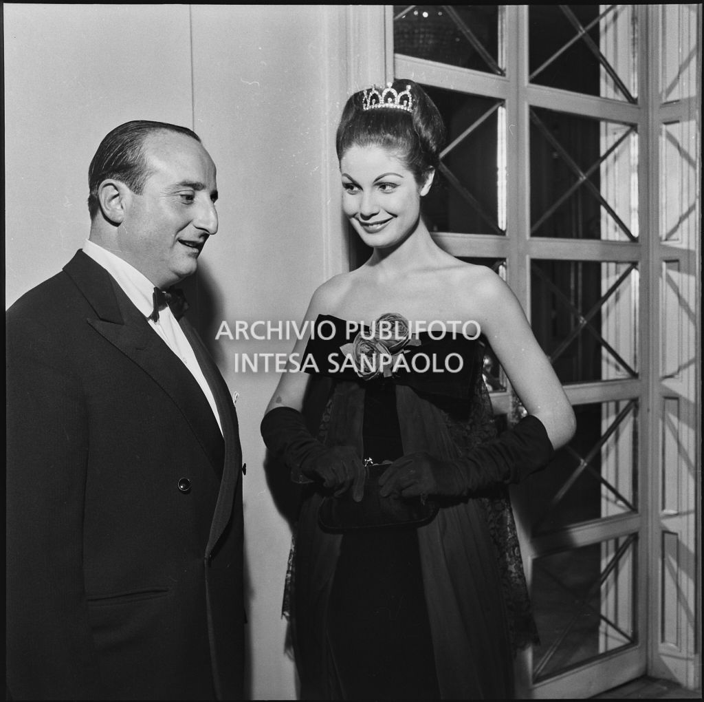 Eletta Polvani in compagnia di un uomo nel foyer del Teatro alla Scala in occasione della serata inaugurale della stagione lirica 1957-1958 con l'opera "Un ballo in maschera", di Giuseppe Verdi, diretta da Gianandrea Gavazzeni con la regia di Margherita Wallmann