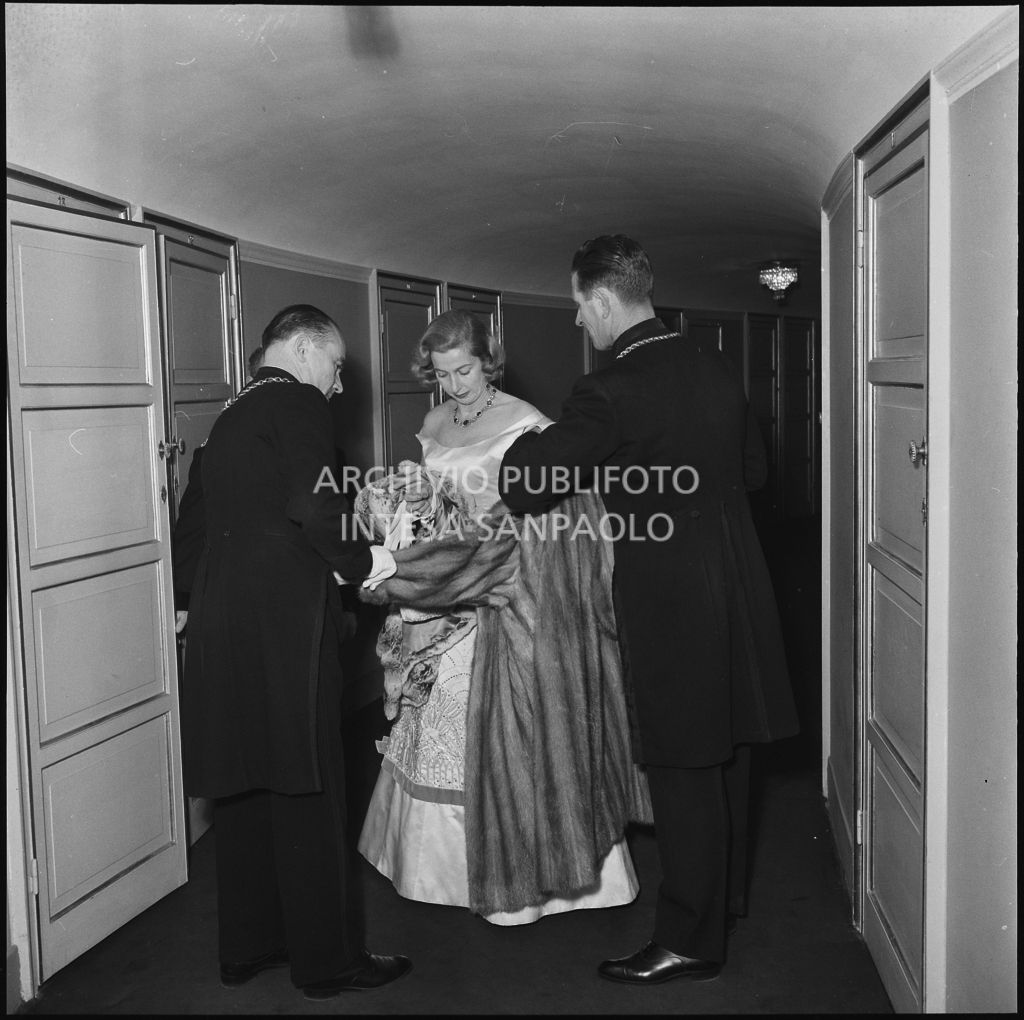 La signora Vassallo aiutata da due maschere del Teatro alla Scala in occasione della serata inaugurale della stagione lirica 1957-1958 del Teatro alla Scala con l'opera "Un ballo in maschera", di Giuseppe Verdi, diretta da Gianandrea Gavazzeni con la regia di Margherita Wallmann