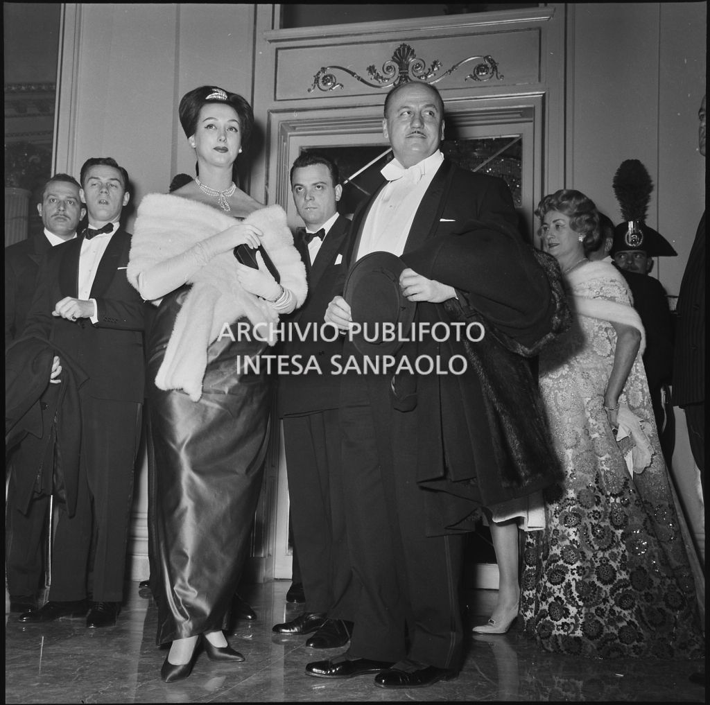 Lo stilista Pierre Balmain e Madeleine Kohler nel foyer del Teatro alla Scala in occasione della serata inaugurale della stagione lirica 1958-1959 con l'opera "Turandot", di Giacomo Puccini, diretta da Antonino Votto con la regia di Margherita Wallmann
