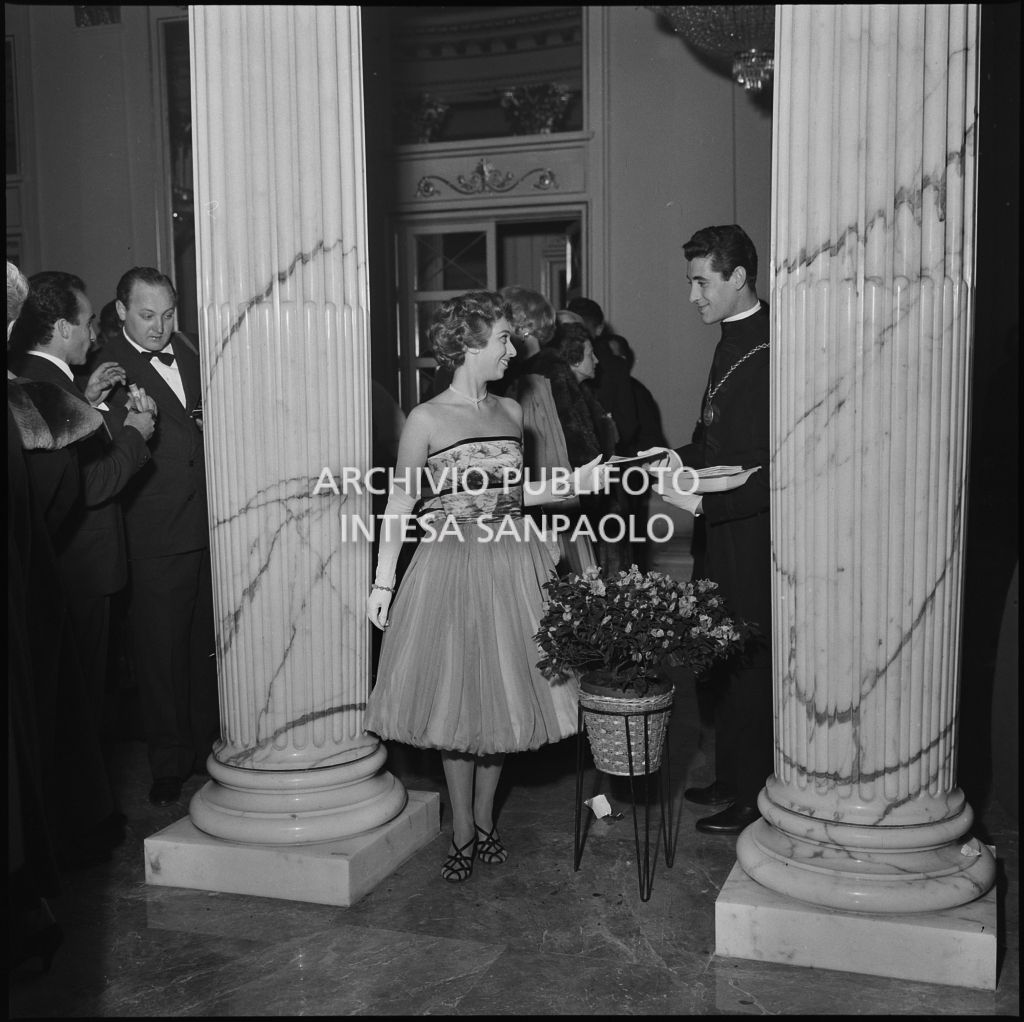 Una spettatrice, nel foyer del Teatro alla Scala, riceve il programma da una maschera in occasione della serata inaugurale della stagione lirica 1958-1959 con l'opera "Turandot", di Giacomo Puccini, diretta da Antonino Votto con la regia di Margherita Wallmann