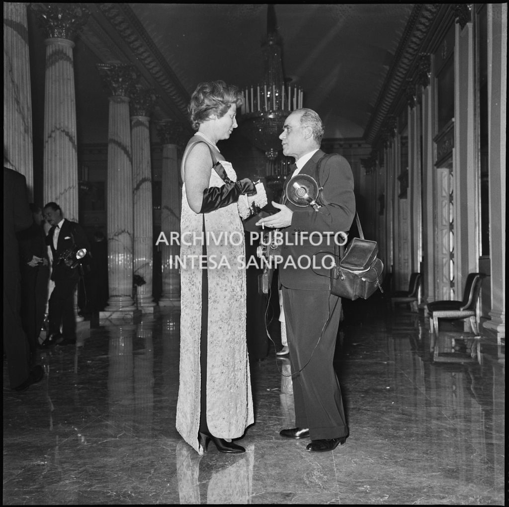 Una spettatrice discute con un fotografo nel foyer del Teatro alla Scala in occasione della serata inaugurale della stagione lirica 1958-1959 con l'opera "Turandot", di Giacomo Puccini, diretta da Antonino Votto con la regia di Margherita Wallmann