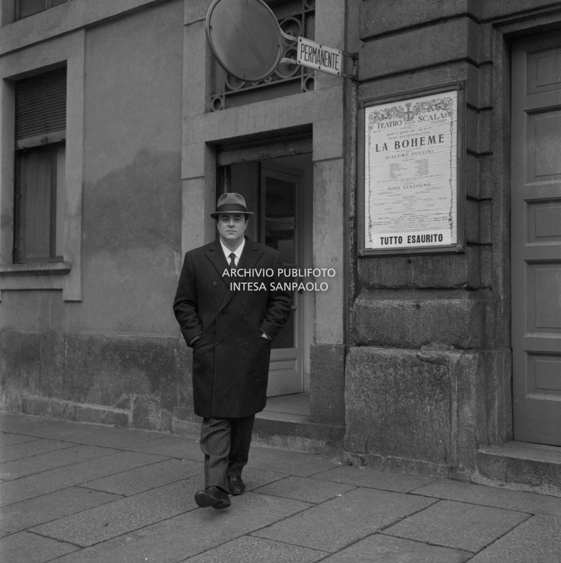 Luciano Pavarotti ritratto a Milano a fianco al Teatro alla Scala; alle sue spalle il cartellone de La Bohème nella quale interpreta Rodolfo