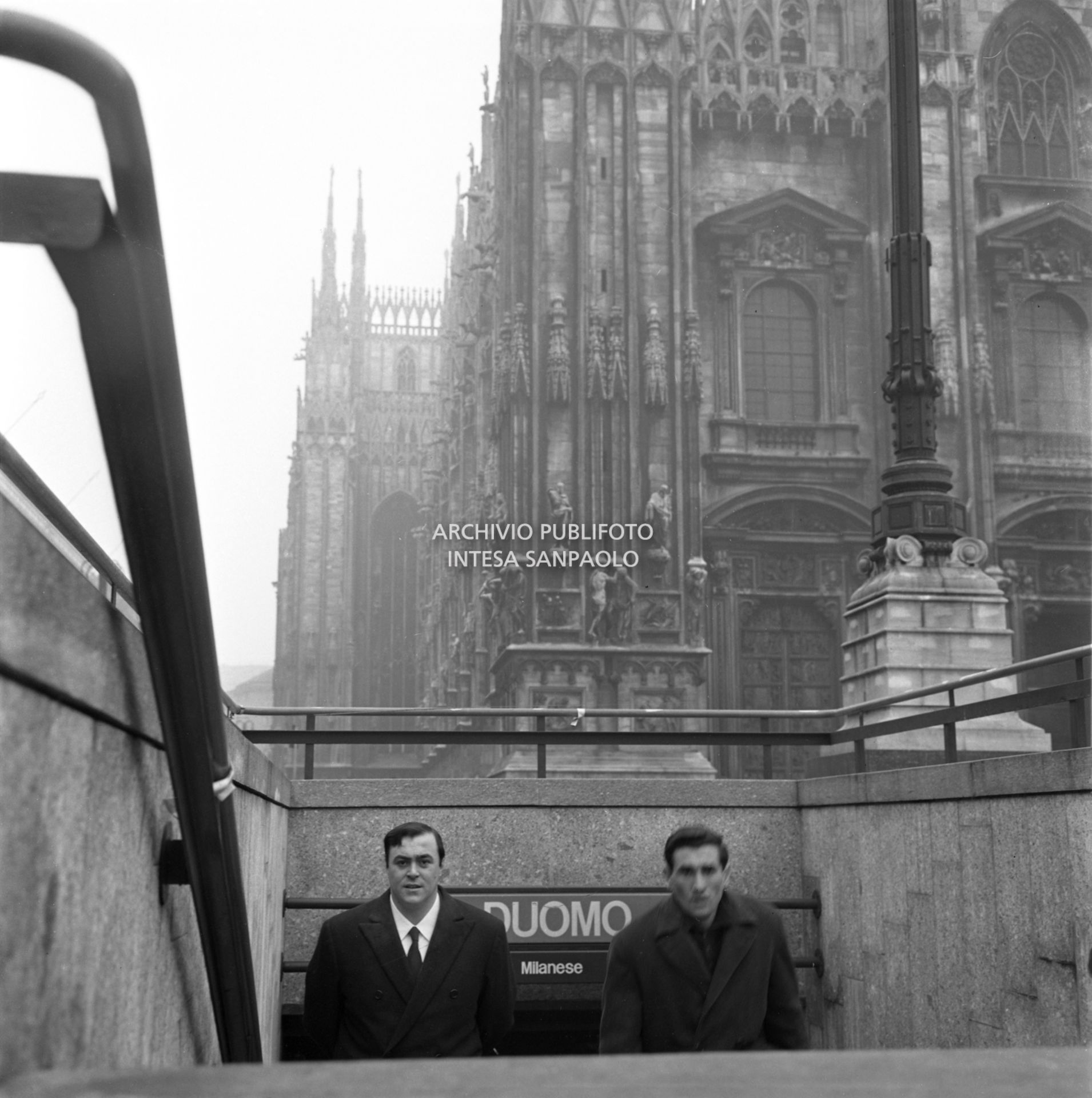 Luciano Pavarotti ritratto sulle scale di ingresso alla stazione Duomo della metropolitana a Milano, sullo sfondo il Duomo