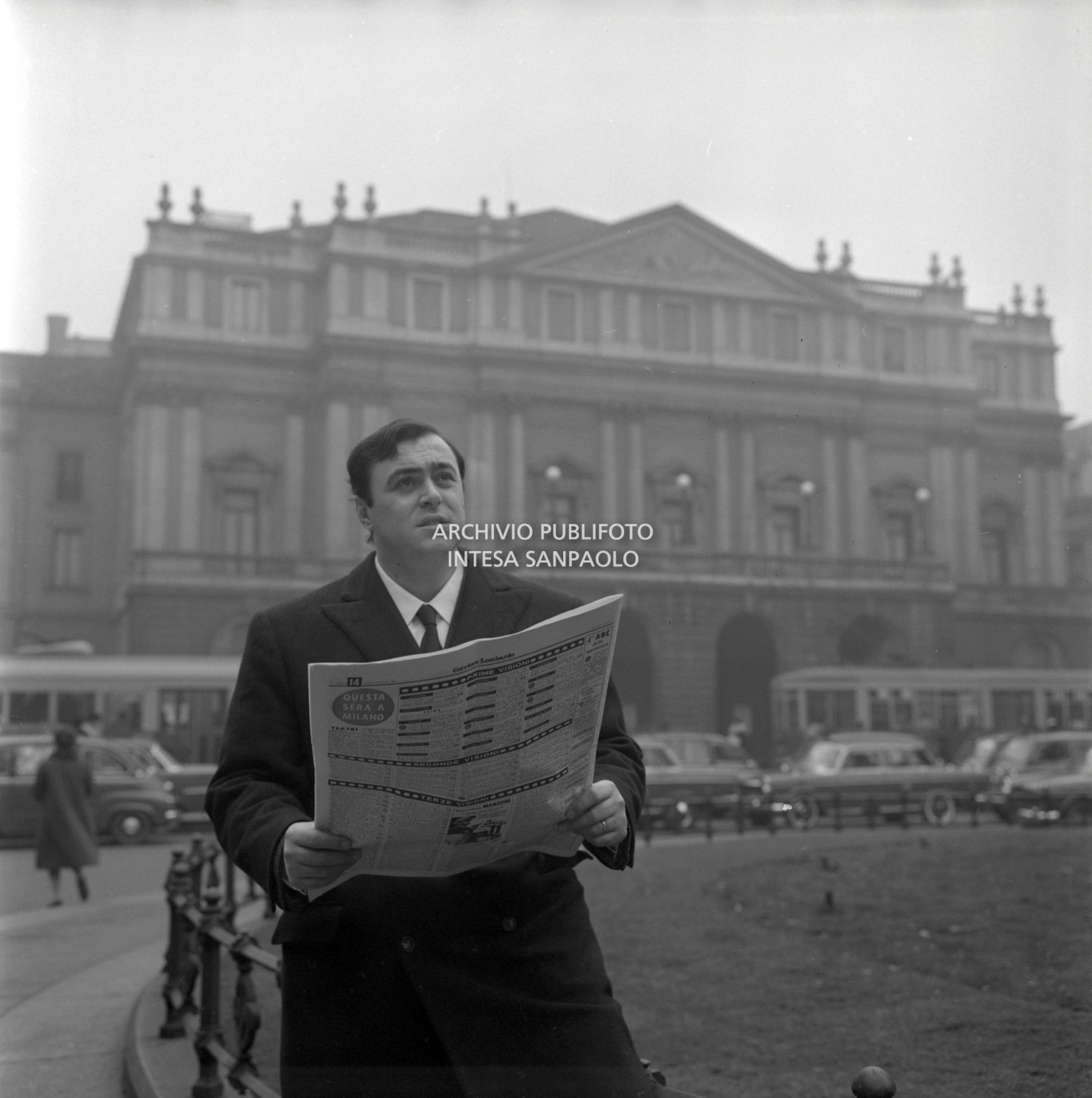 Luciano Pavarotti, ritratto in piazza della Scala a Milano, con Il Corriere Lombardo; alle sue spalle il Teatro alla Scala