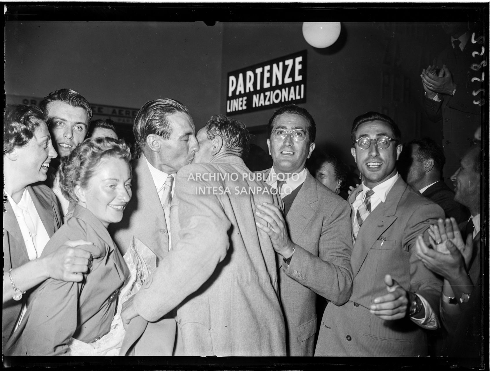 Ubaldo Rey (che sta baciando un uomo) con la moglie (in primo piano) tra la folla che accoglie gli alpinisti di ritorno dalla spedizione sul K2 all'aeroporto Linate a Milano