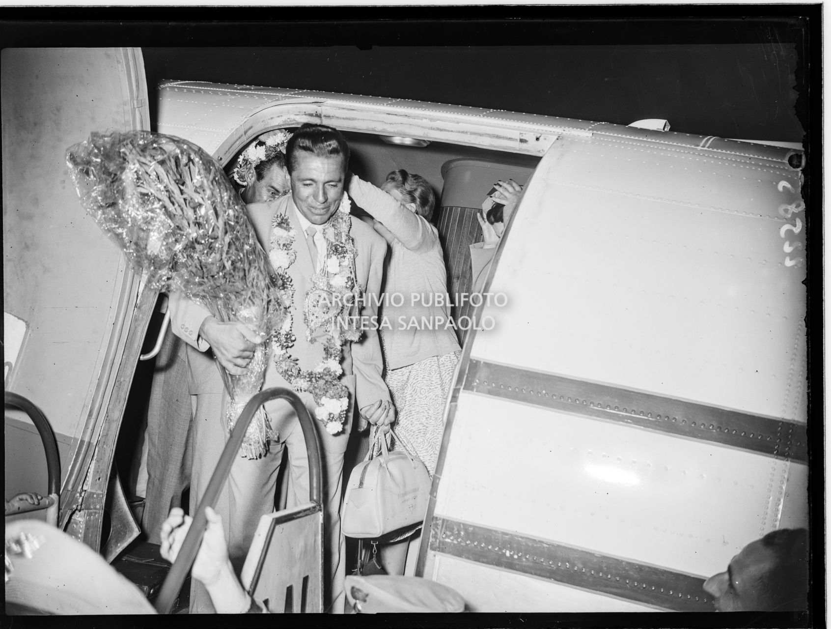 Discesa di Achille Compagnoni dall'aereo con cui lui e altri membri della spedizione sono appena atterrati all'aeroporto Linate a Milano, accolti dalla folla festante