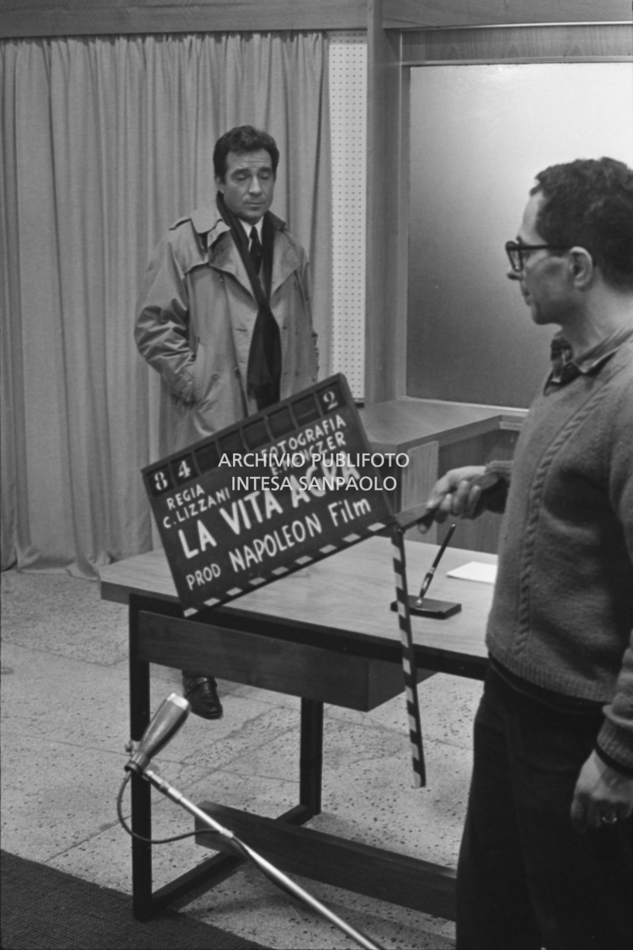 Ugo Tognazzi sul set del film "La vita agra" alla Fiera Campionaria a Milano; in primo piano il ciak