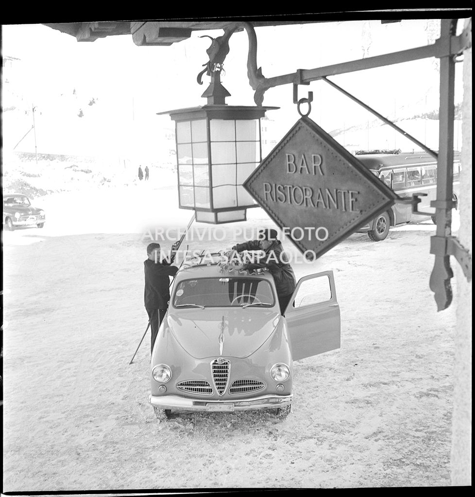 Due uomini caricano alcuni sci sul tetto di un'Alfa Romeo 1900