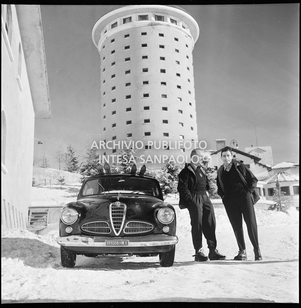 Giuseppe "Nino" Farina e Fausto Coppi a fianco a un'Alfa Romeo 1900; alle loro spalle l'Hotel La Torre al Sestriere