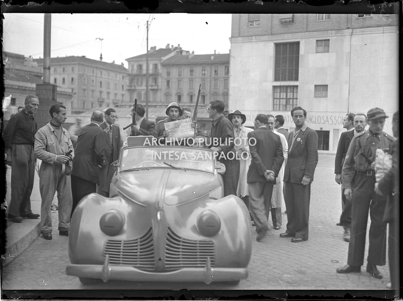 Membri del Corpo Volontari della Libertà a Milano nella prima giornata dell'insurrezione generale a Milano; un uomo mostra la prima pagina del giornale "L'Italia Libera" che titola "Insurrezione nazionale"