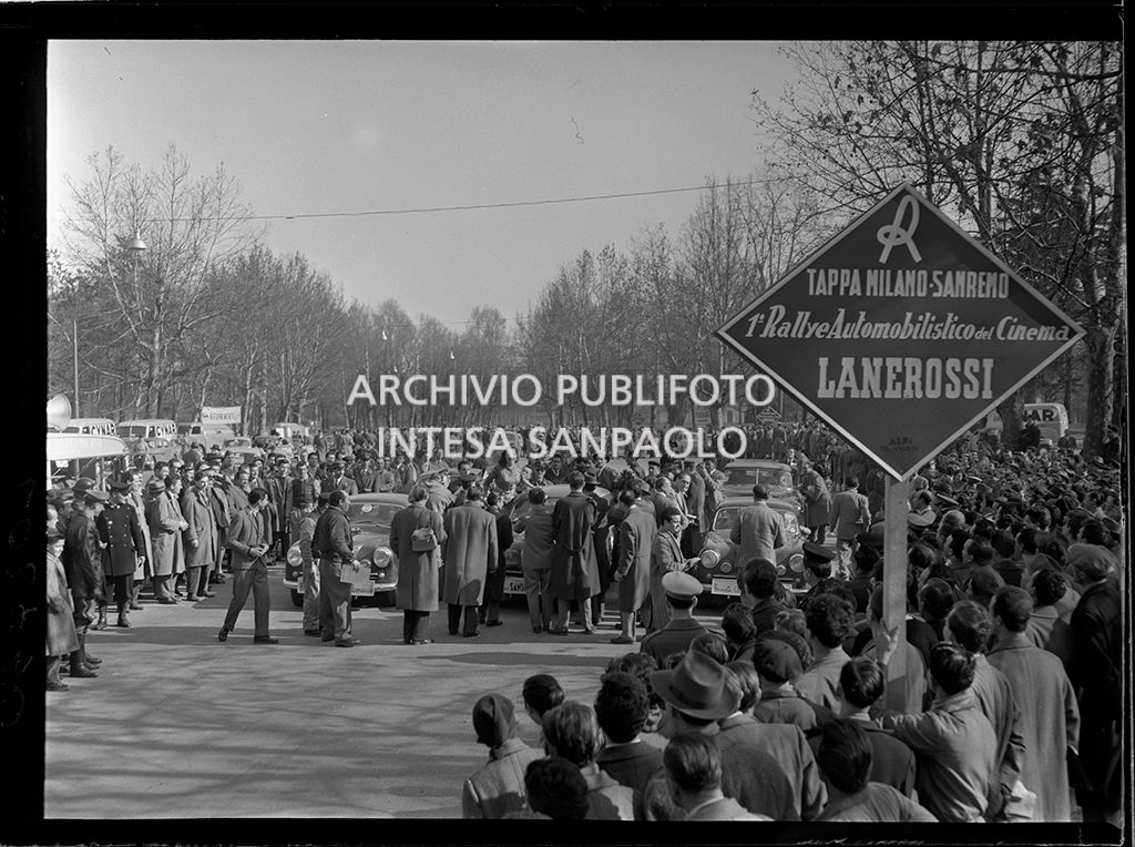 Partenza della tappa Milano-Sanremo del 1° Rallye automobilistico del cinema promosso da Lanerossi: folla intorno alla Alfa Romeo 1900 con cui gareggiano Yvonne Sanson, visibile tra la folla, e Paolo Marzotto