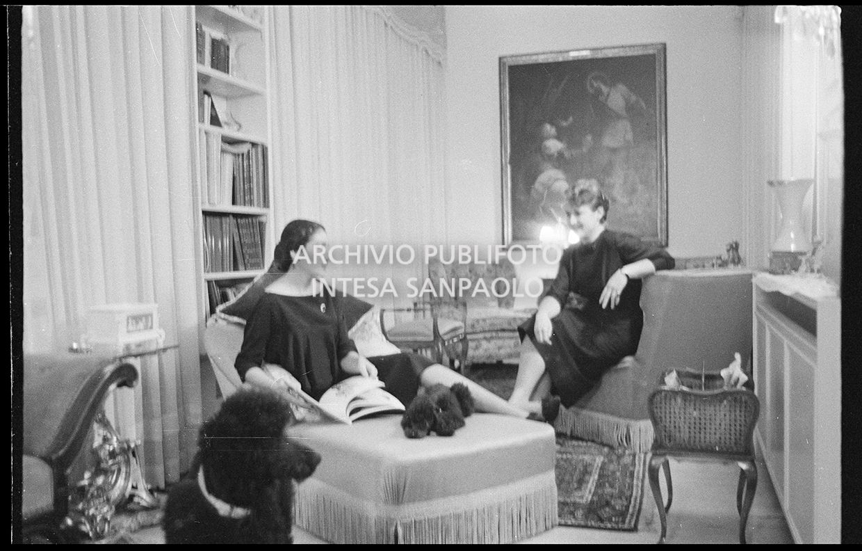 Maria Callas seduta sulla chaise longue in compagnia della segretaria e dei suoi barboncini