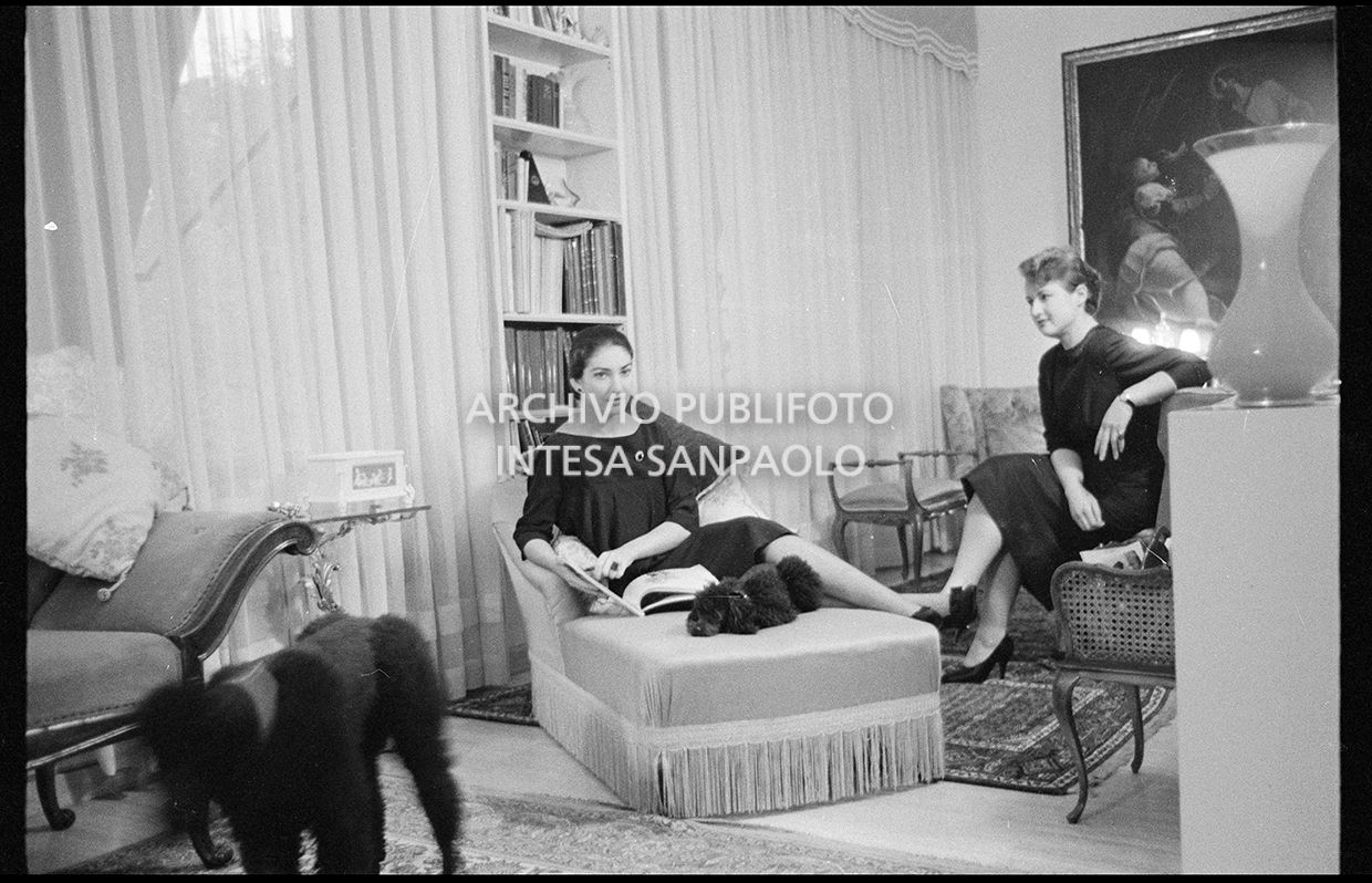 Maria Callas seduta sulla chaise longue in compagnia della segretaria e dei suoi barboncini
