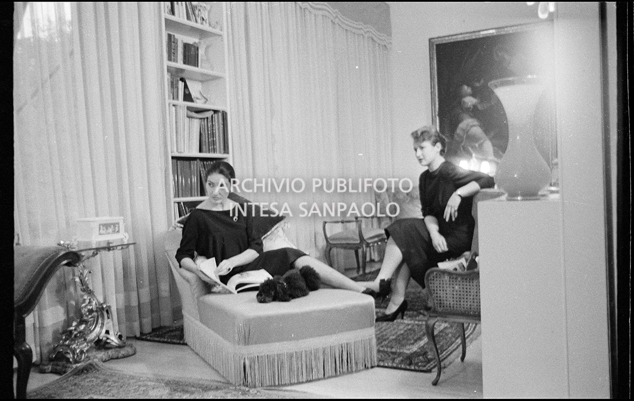 Maria Callas seduta sulla chaise longue in compagnia della segretaria e del suo barboncino