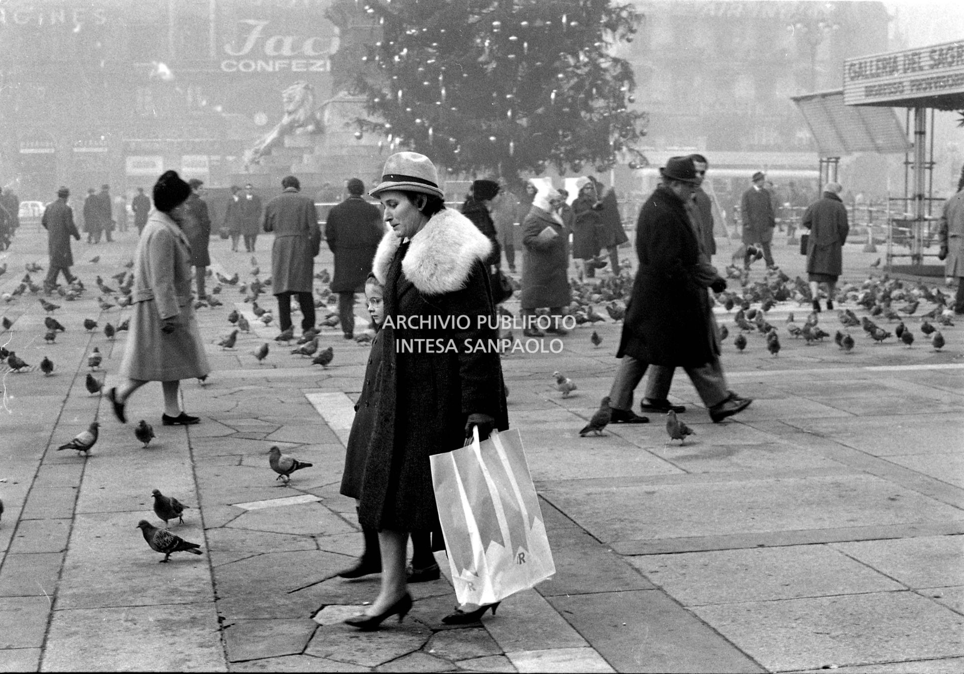 Passanti i in piazza del Duomo a Milano; sullo sfondo l'albero di Natale