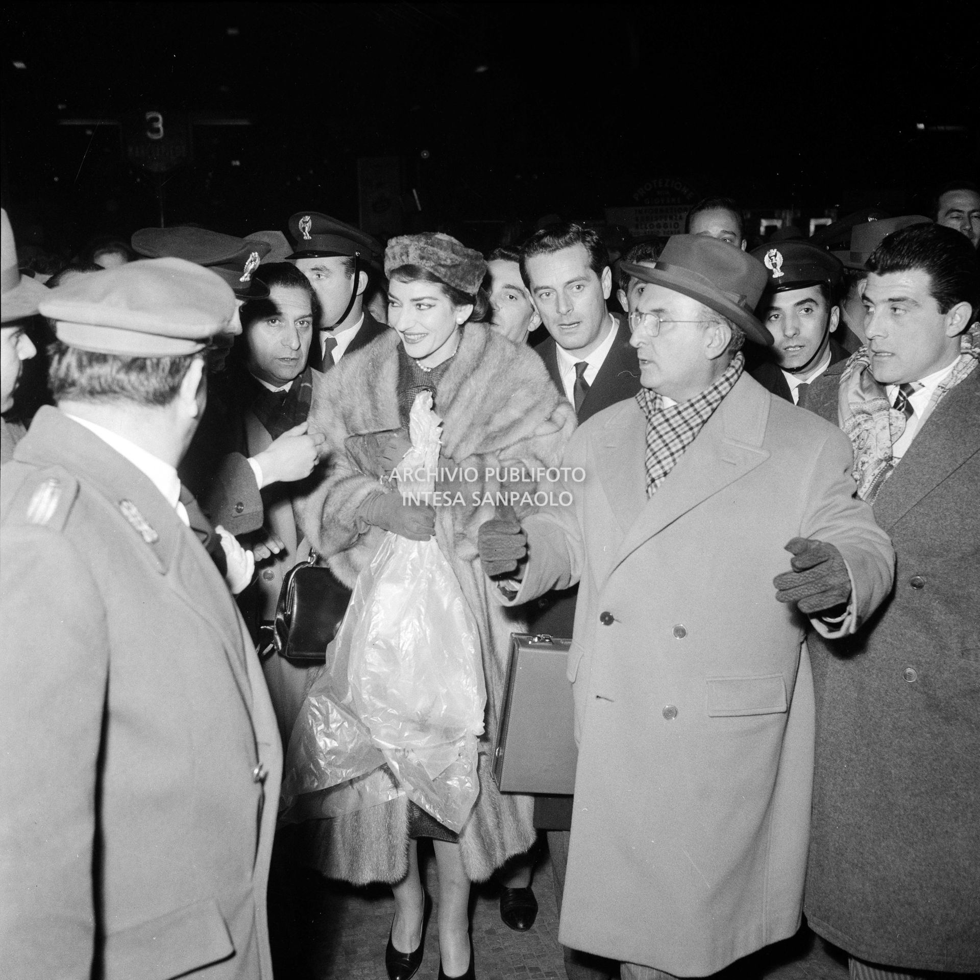 Maria Callas alla Stazione Centrale di Milano, al suo rientro da Roma, si fa strada tra la folla accorsa per accoglierla, con un mazzo di fiori tra le mani