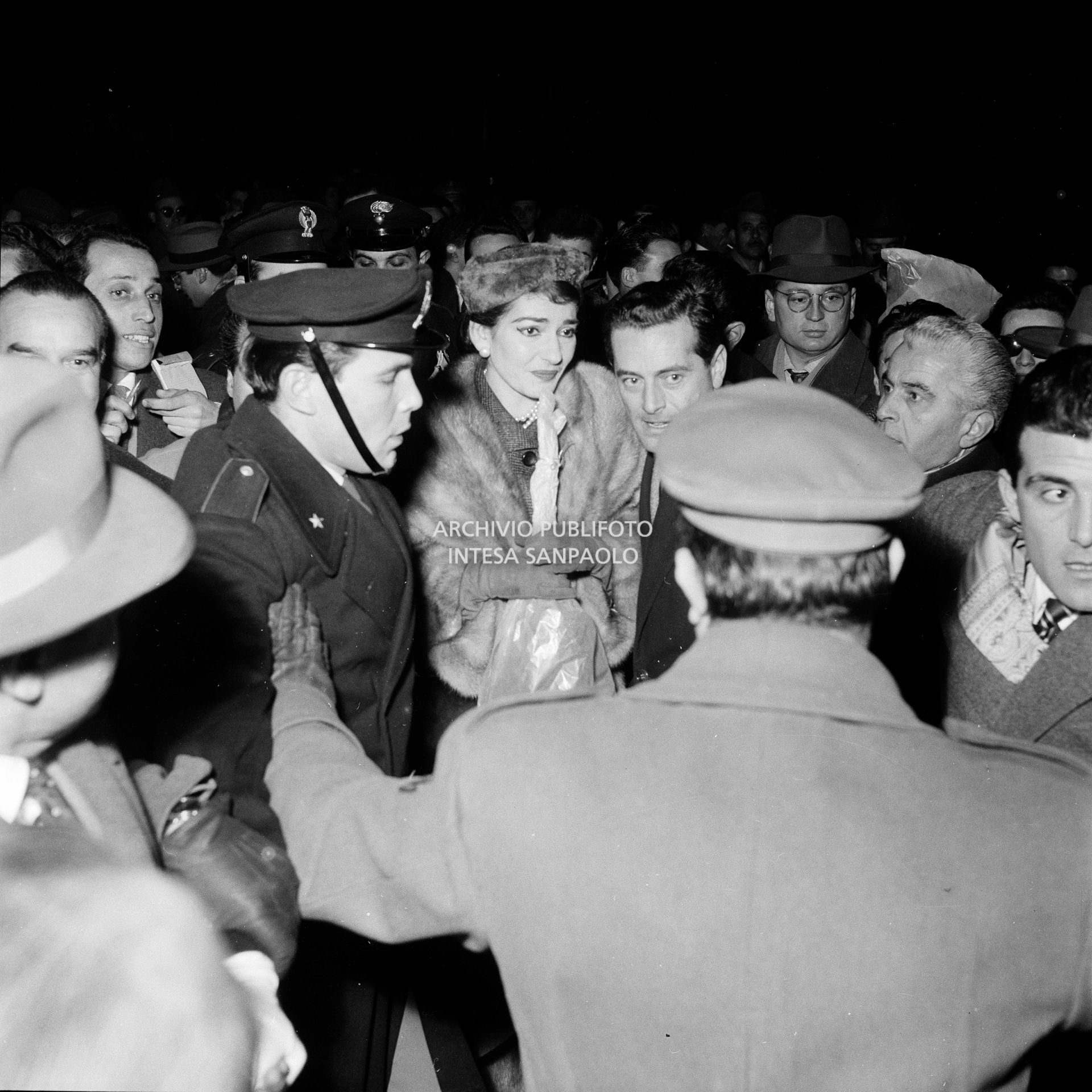 Maria Callas alla Stazione Centrale di Milano, al suo rientro da Roma, si fa strada tra la folla accorsa per accoglierla, con un mazzo di fiori tra le mani