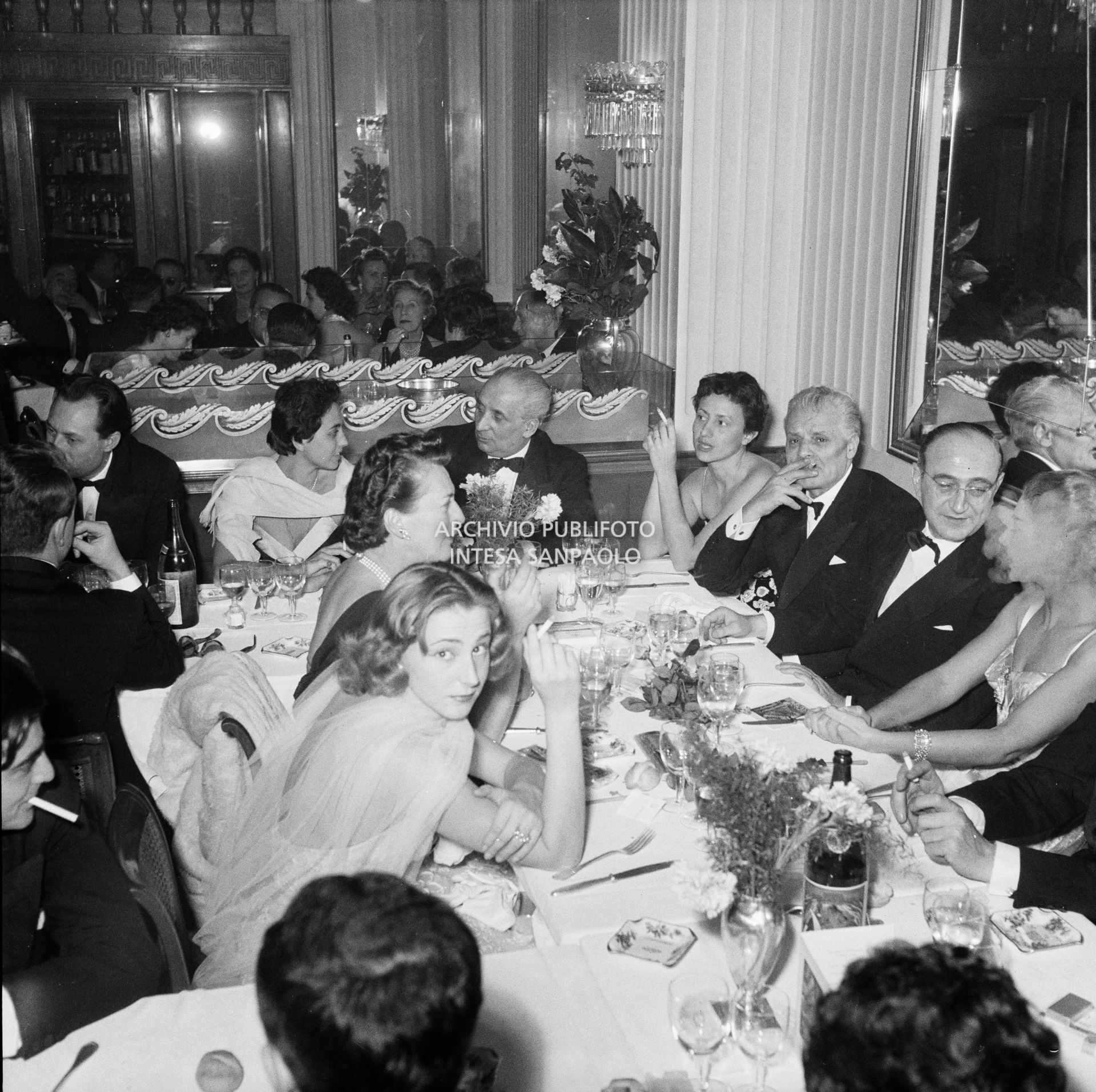 Maria Callas a cena al ristorante Savini di Milano, la sera della Prima della Vestale di Gaspare Spontini. Alla sua sinistra il regista Luchino Visconti, di fronte a lei Emanuela di Castelbarco Toscanini, a capo tavola il marito Giovanni Battista Meneghini, e quinto da destra il soprintendente del Teatro alla Scala Antonio Ghiringhelli