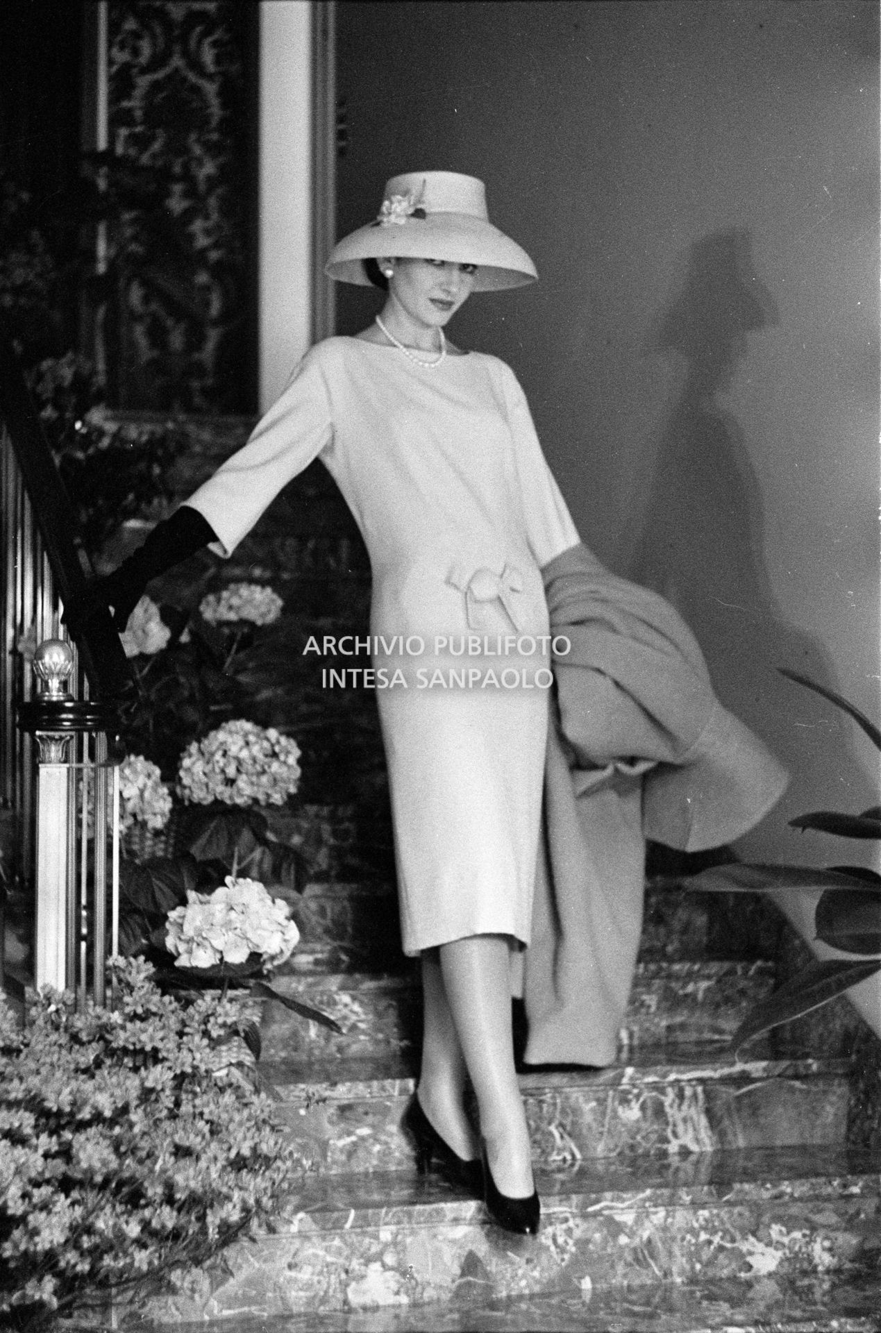 Maria Callas, ritratta in posa sulle scale della sua abitazione, indossa abito e cappello della sartoria Biki