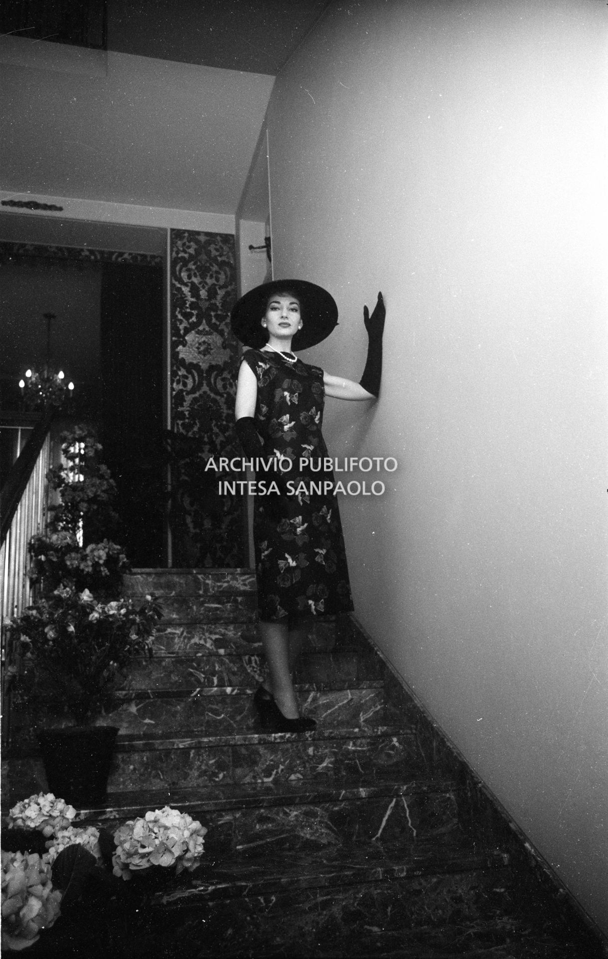 Maria Callas, ritratta in posa sulle scale della sua abitazione, indossa abito e cappello della sartoria Biki