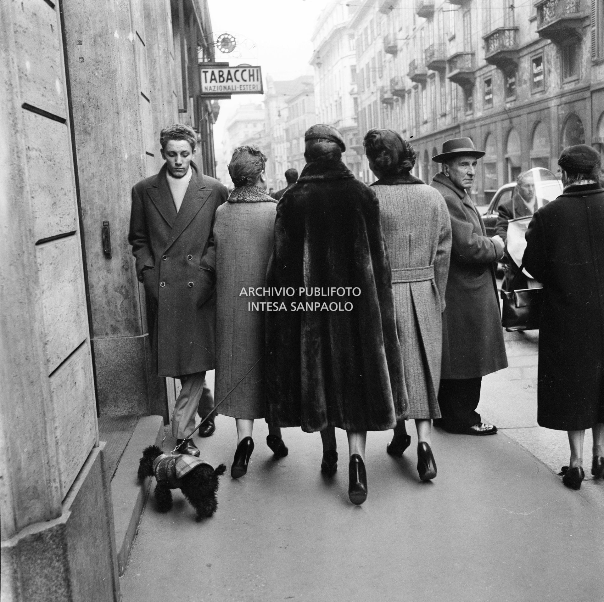 Maria Callas ripresa di spalle mentre passeggia con il suo barboncino in compagnia dell'amica Giovanna Lomazzi, a destra, e della sua segretaria, in via Manzoni a Milano