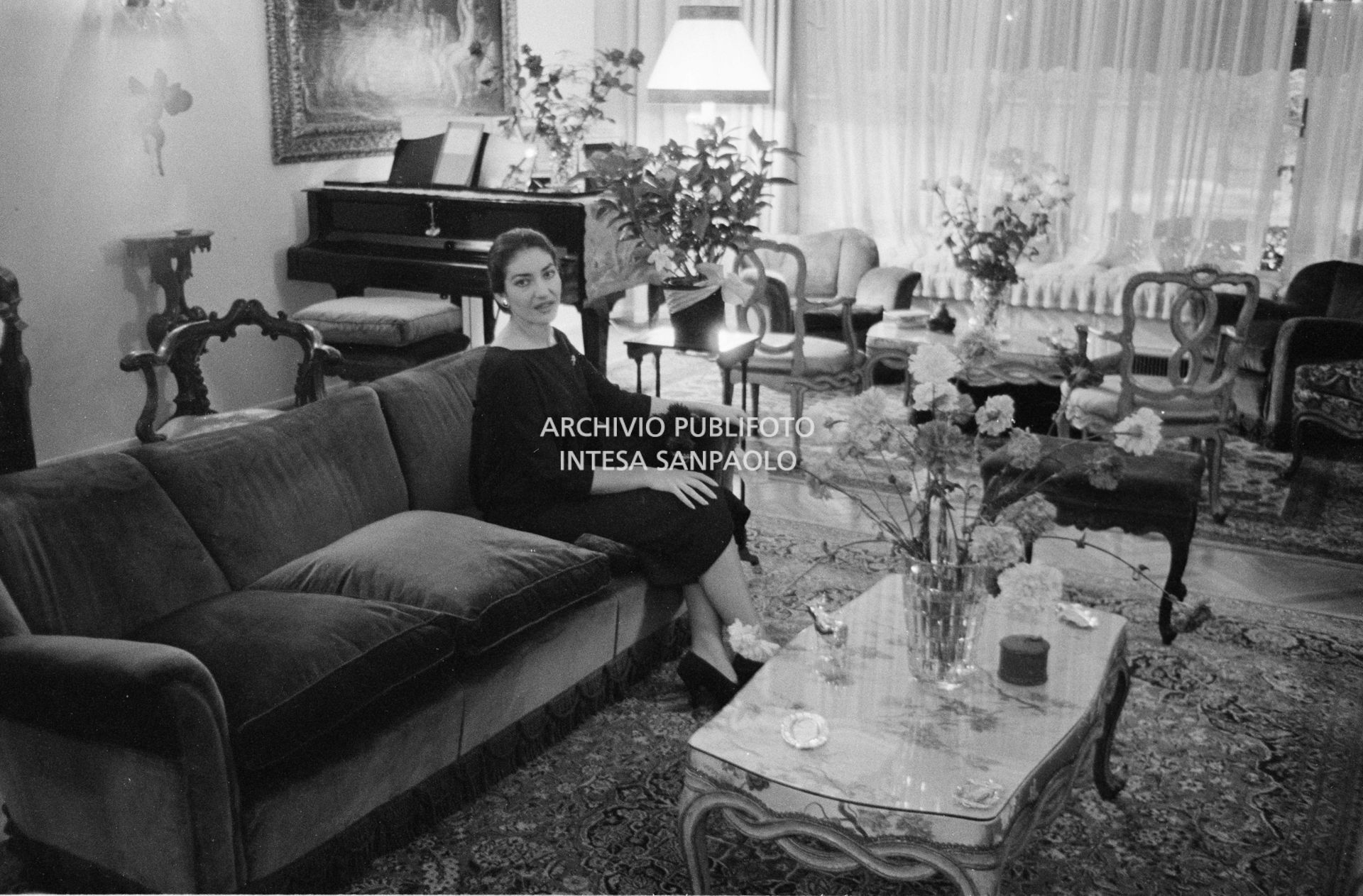 Maria Callas, ritratta nella sua abitazione, seduta sul divano in salotto con uno dei suoi cani