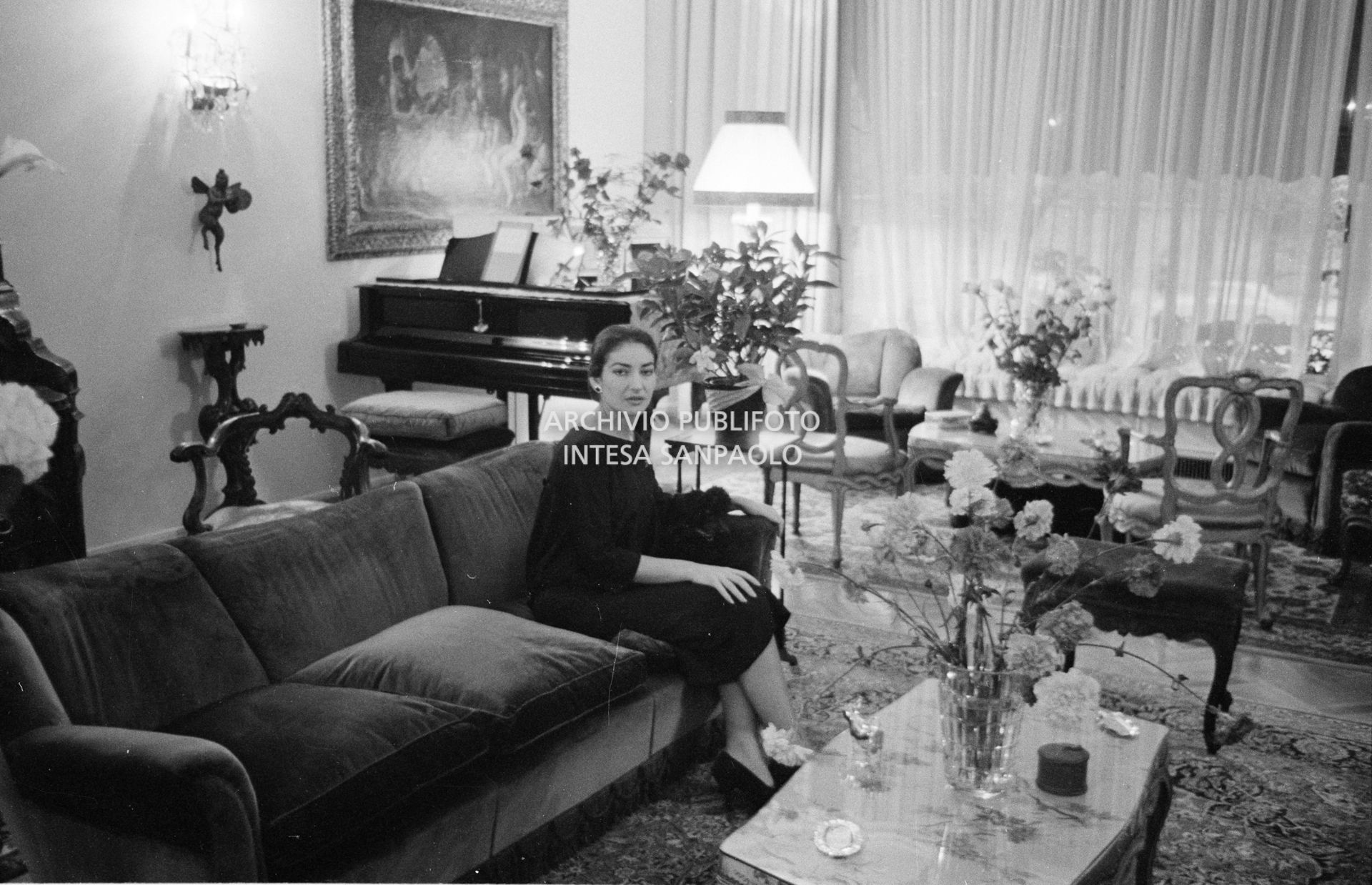 Maria Callas, ritratta nella sua abitazione, seduta sul divano in salotto con uno dei suoi cani