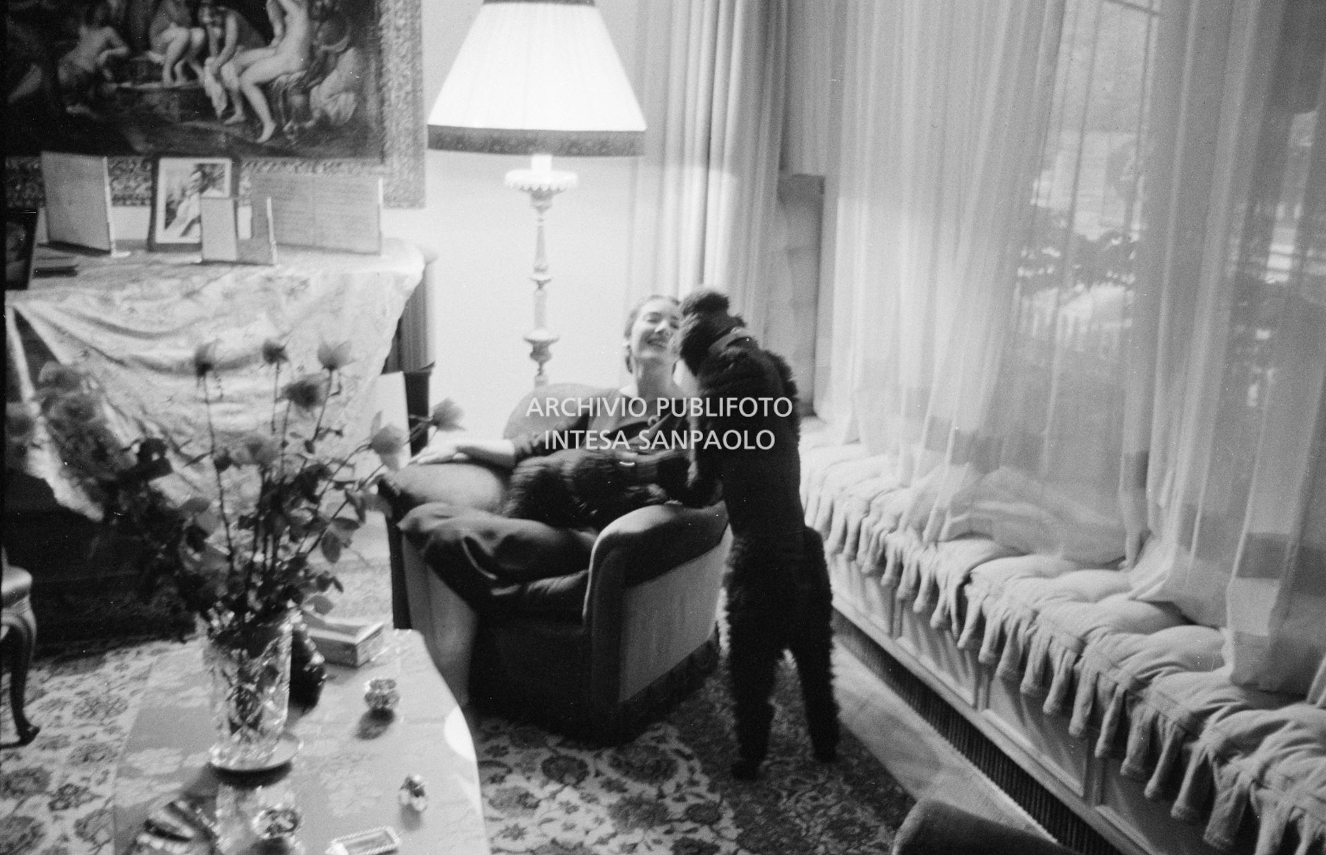 Maria Callas seduta in poltrona, nel salotto della sua abitazione, gioca con i suoi cani