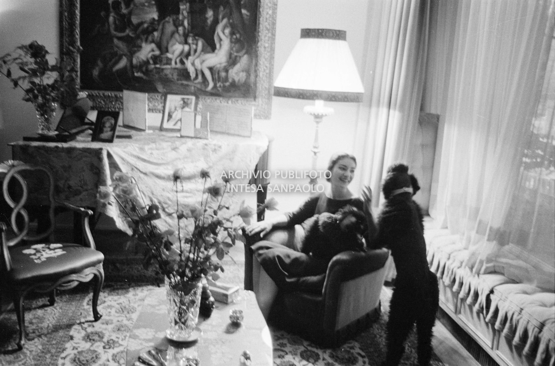 Maria Callas seduta in poltrona, nel salotto della sua abitazione, gioca con i suoi cani
