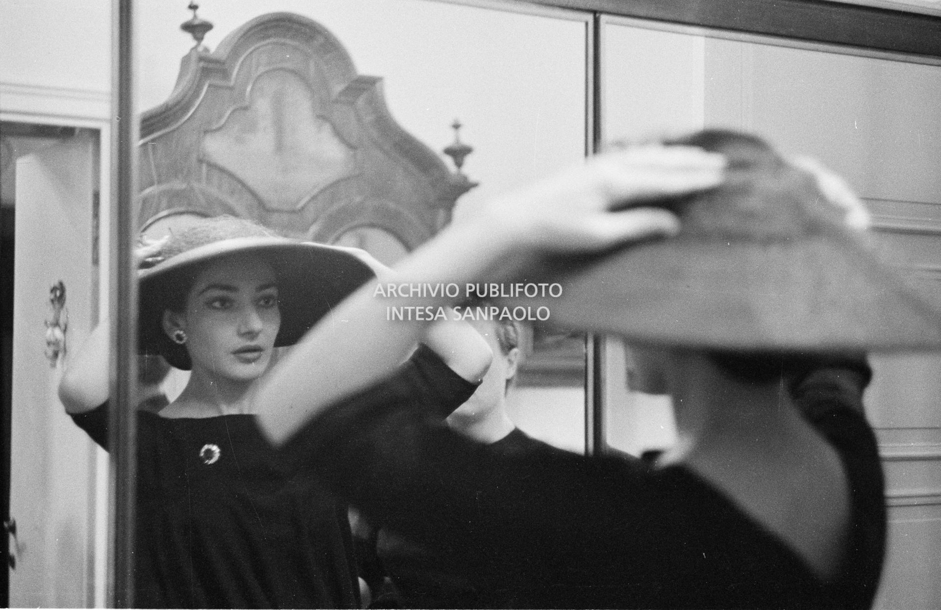 Maria Callas, ritratta nella sua abitazione, si sistema il cappello della sartoria Biki allo specchio